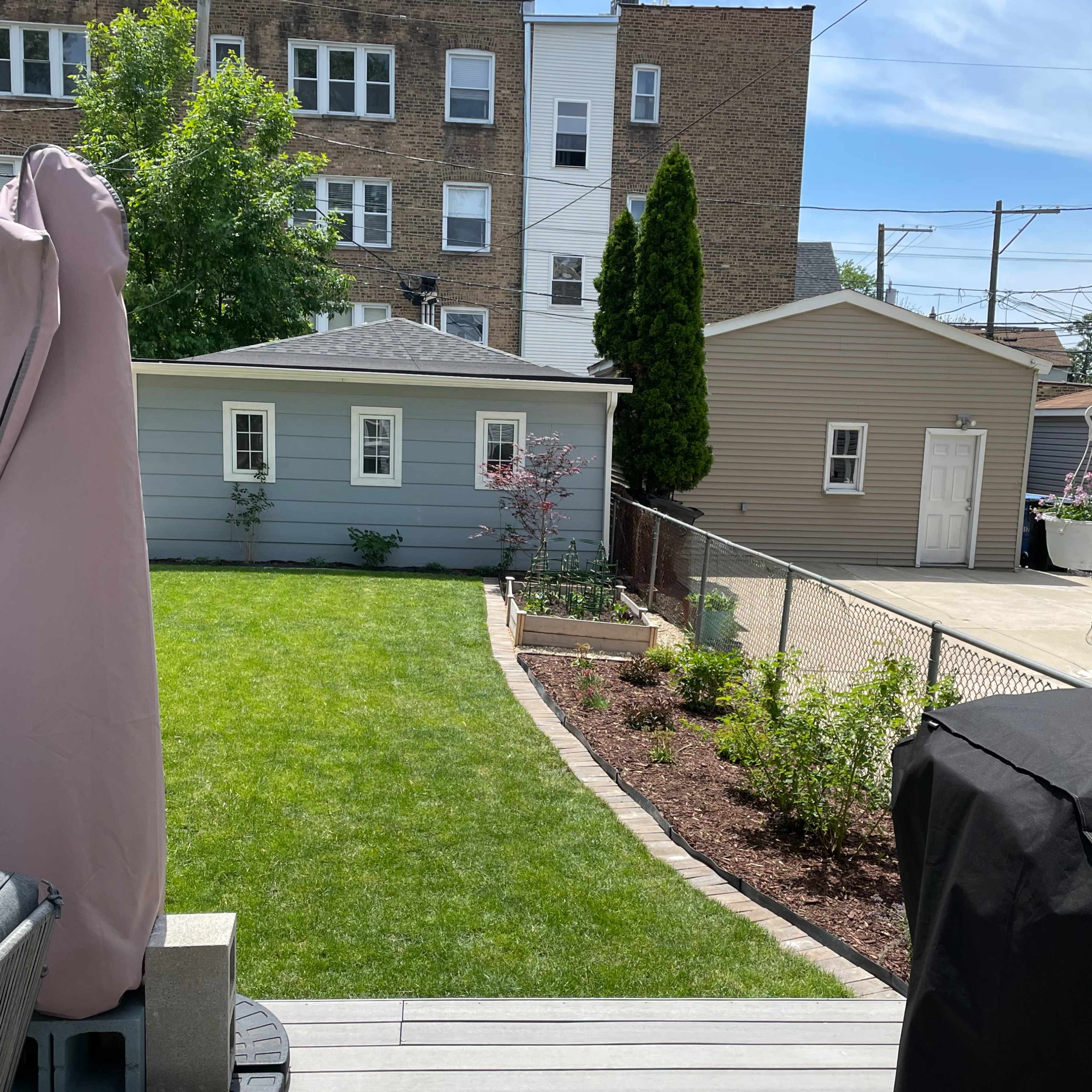 A well-maintained backyard with a lawn, flower beds, and a small shed in the background.