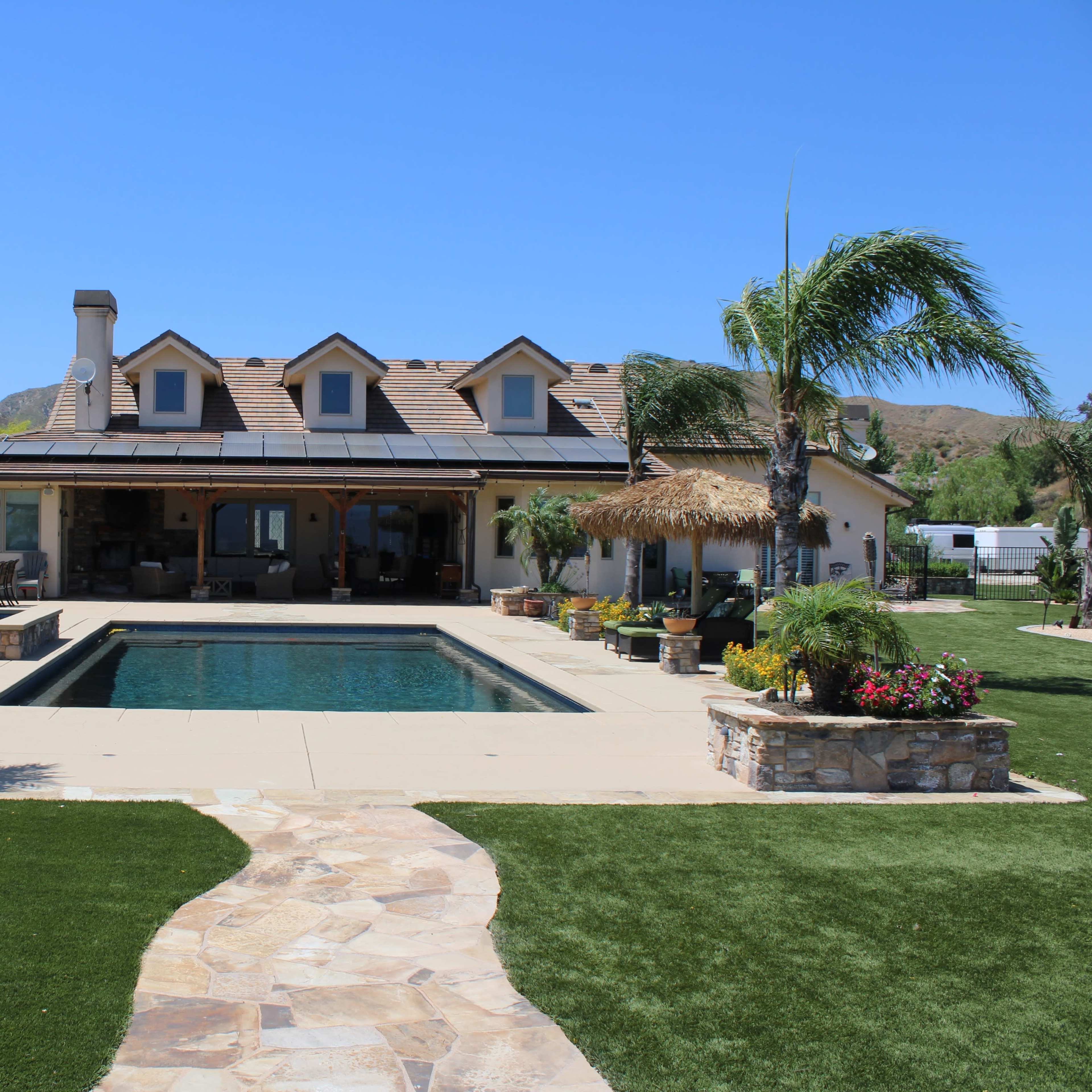 A single-story house with a pool and landscaped garden features a stone pathway leading to the entrance.