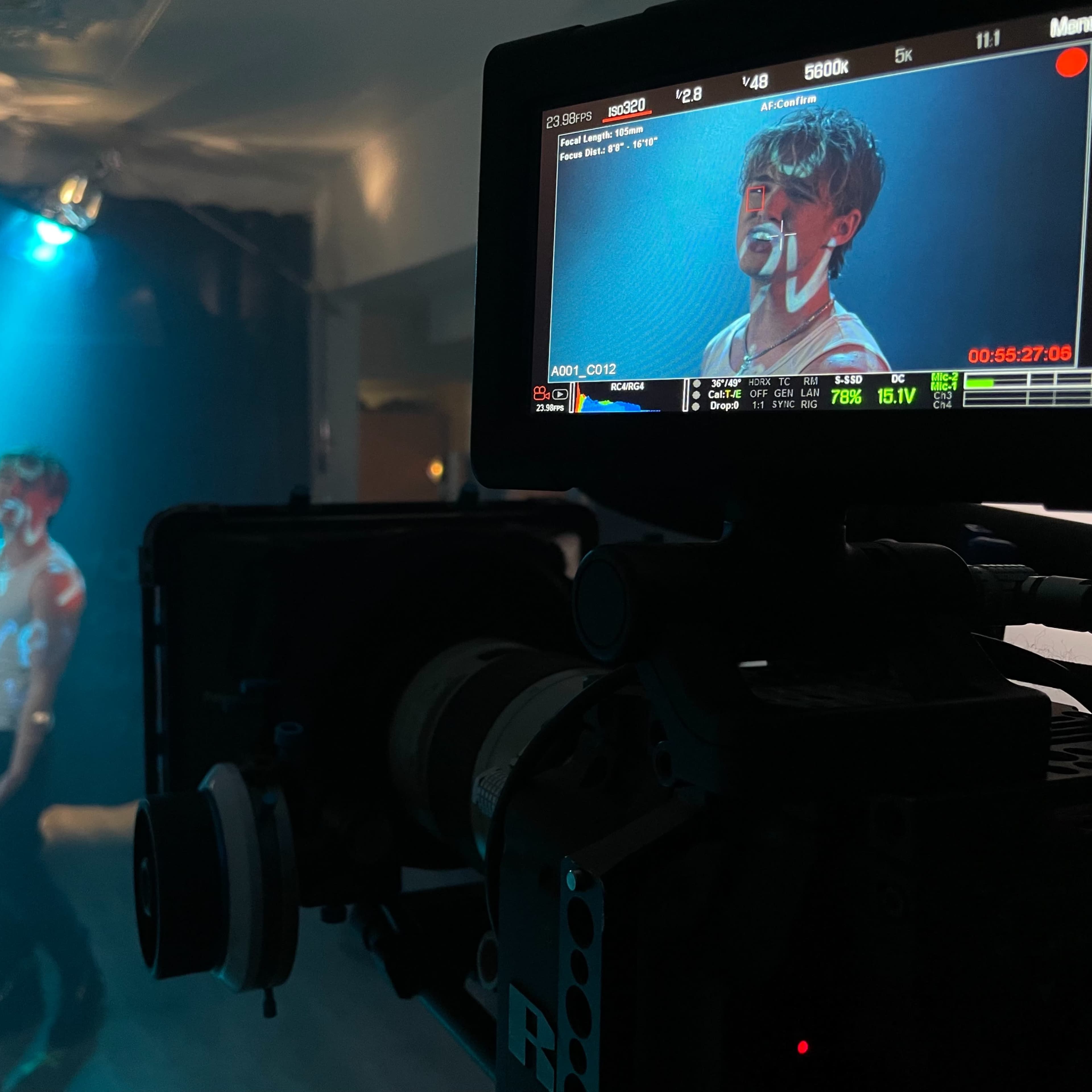 A camera focuses on a performer in a dimly lit room with a spotlight shining on them.