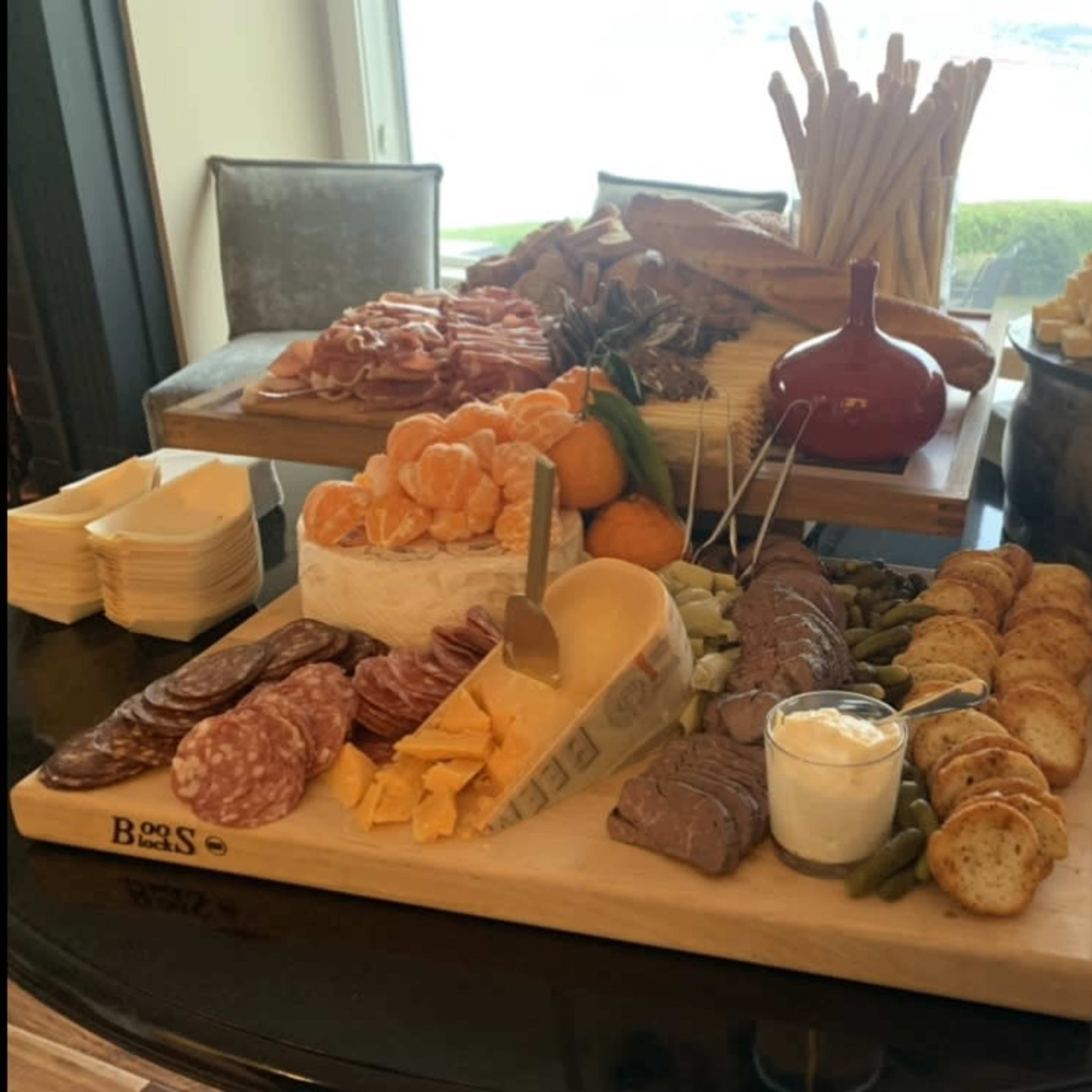 A large charcuterie board is displayed featuring various meats, cheeses, fruits, and bread alongside a bowl of dip.