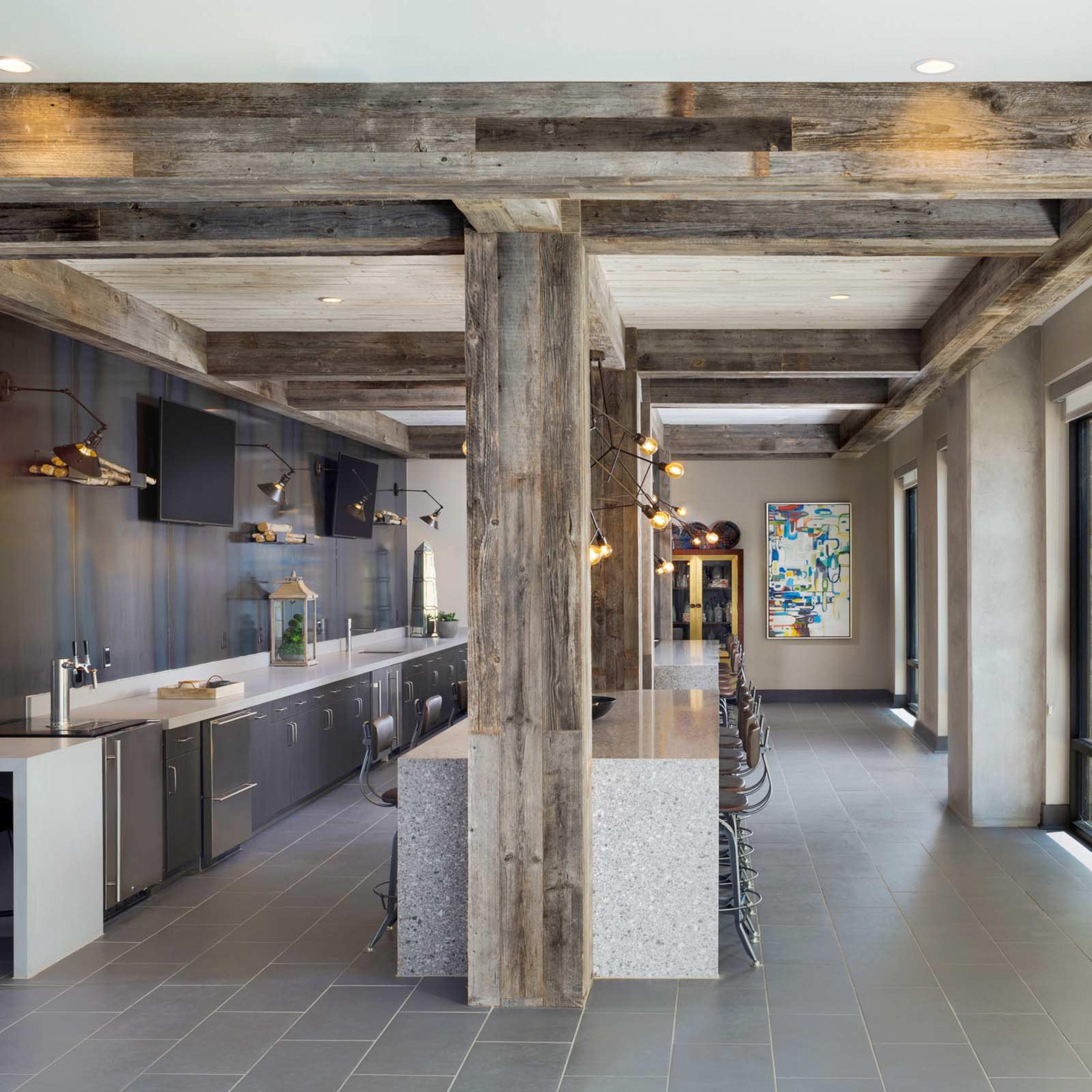 A modern kitchen and dining area with a long, sleek counter, industrial-style lighting, and large windows overlooking an outdoor space.