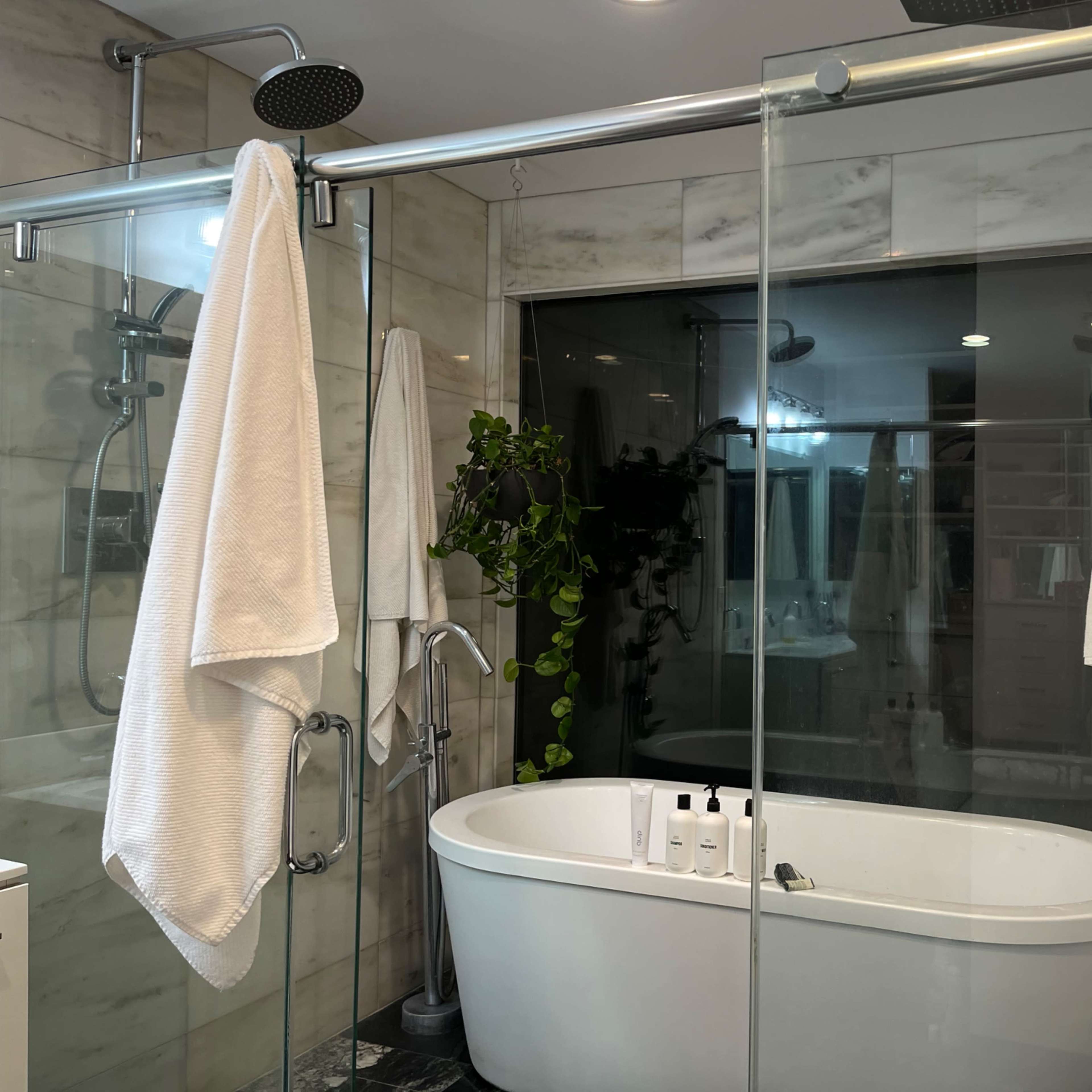 A modern bathroom featuring a freestanding bathtub, a glass-enclosed shower area, and white towels hanging on glass panels.