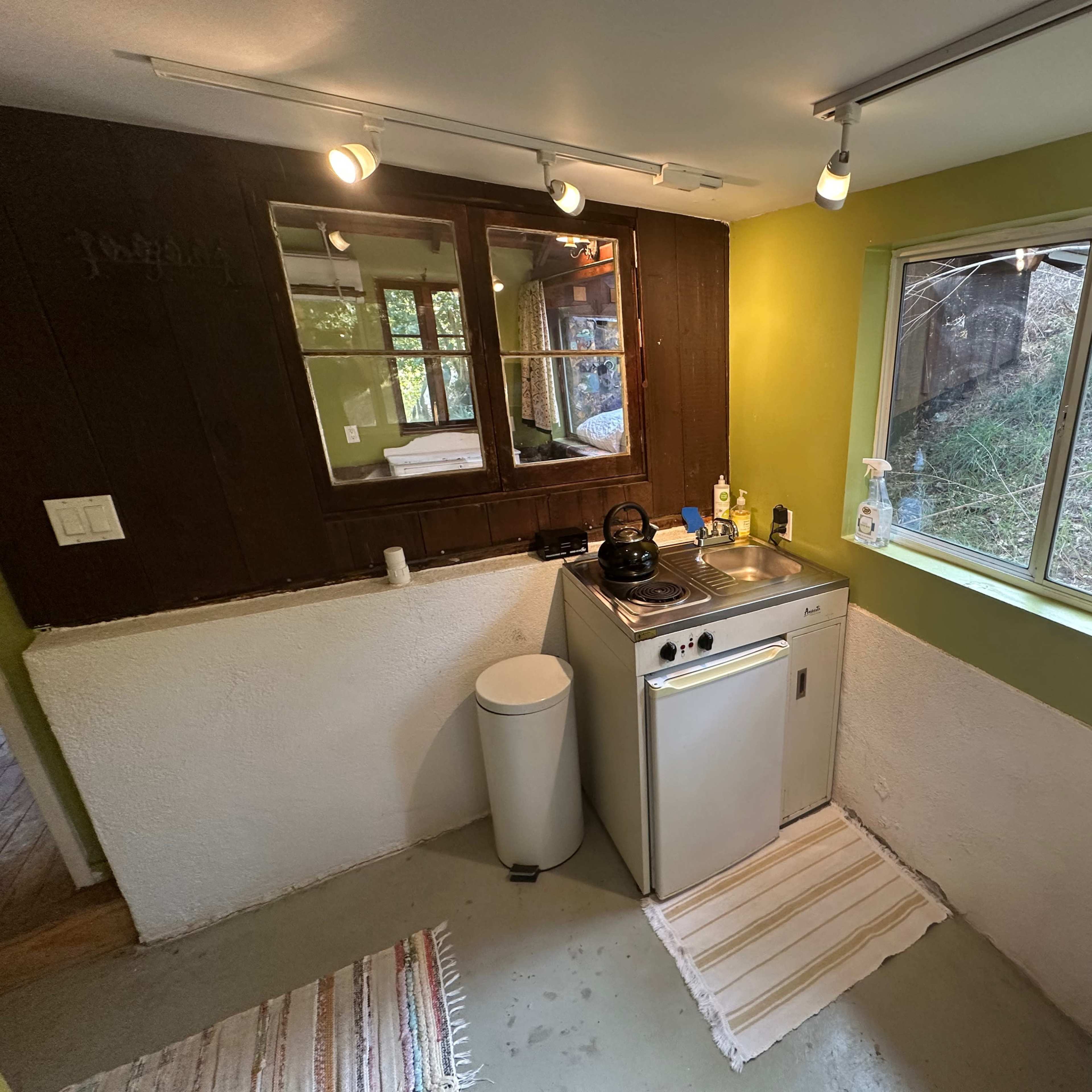 A small kitchen area with a sink, stove, and window overlooking a wooded landscape.