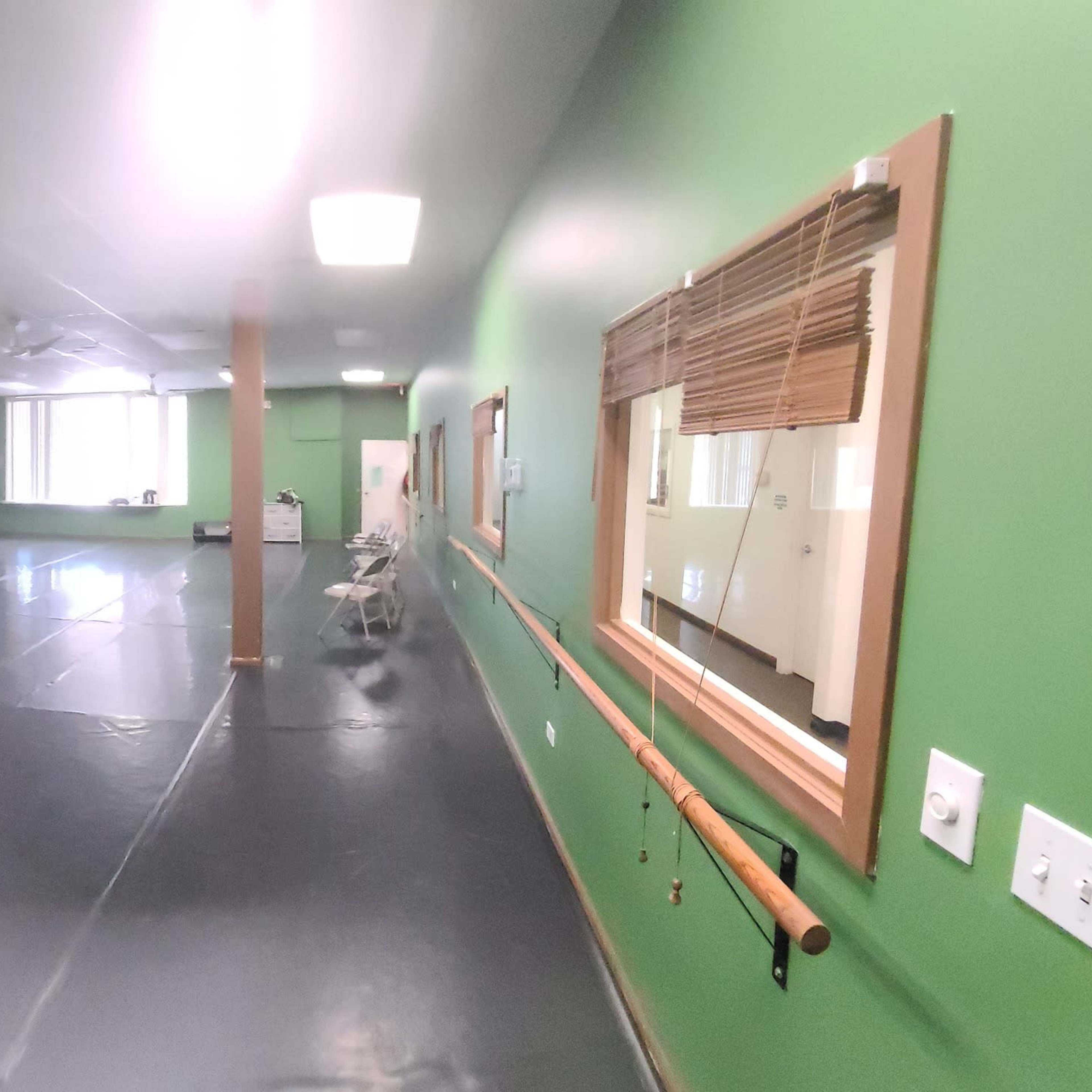 A spacious dance studio with green walls, a mirrored wall, and ballet barres lining the sides.