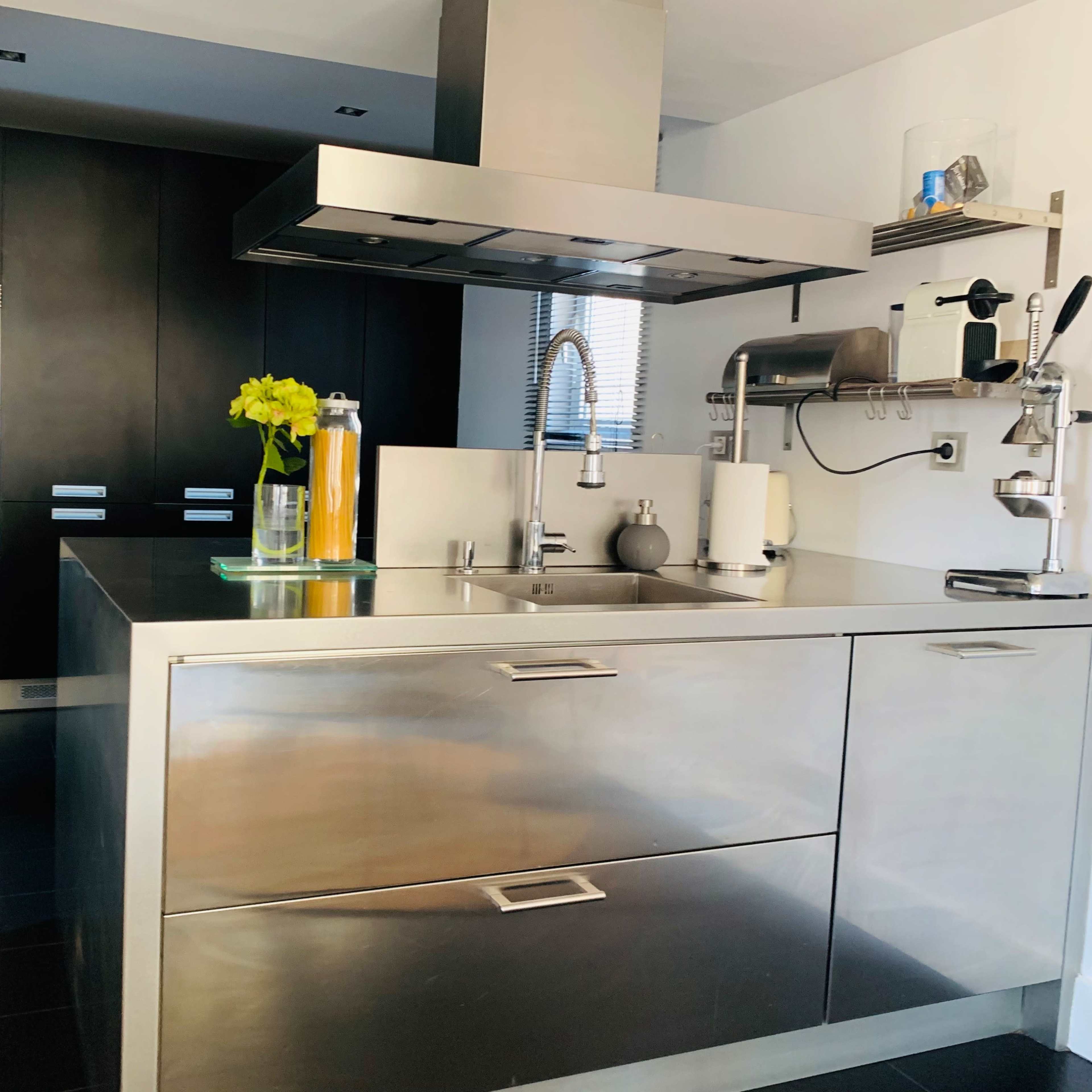 A modern kitchen with a stainless steel island, a hood above a cooktop, and dark cabinetry in the background.