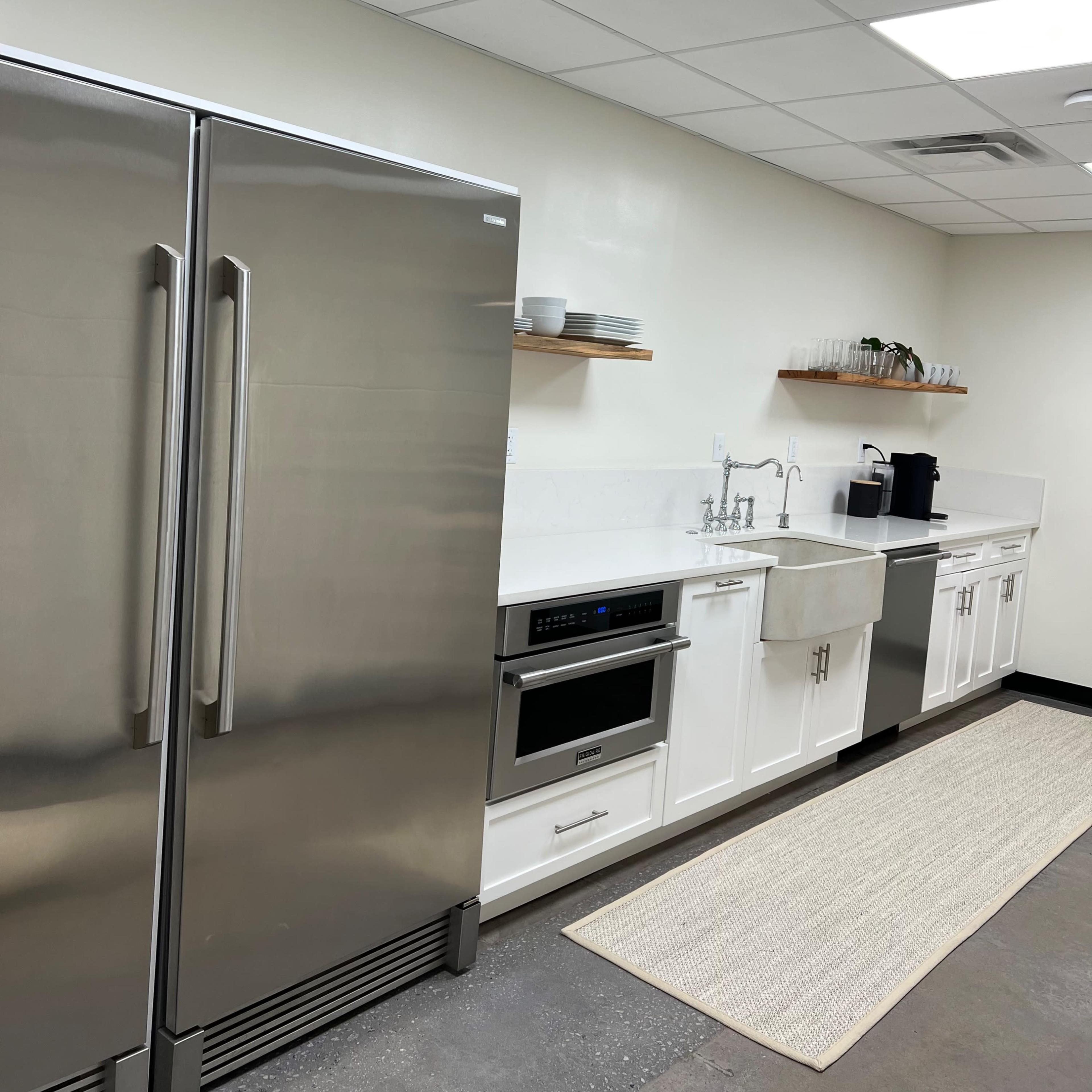 A modern kitchen features stainless steel appliances, white cabinetry, and a sink, with a rug on the floor and shelves holding dishes above.