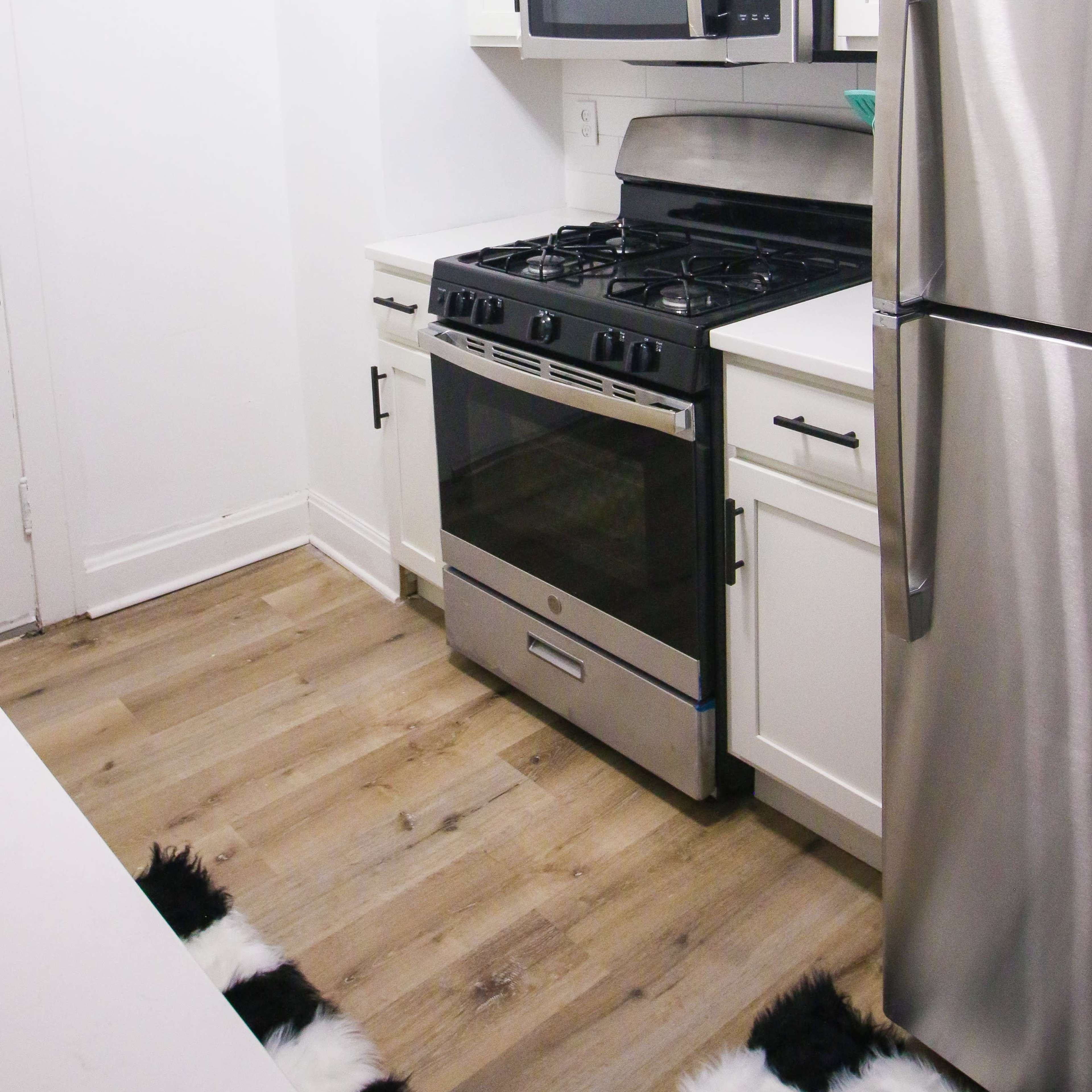 A modern kitchen with white cabinets, stainless steel appliances, and wooden flooring.