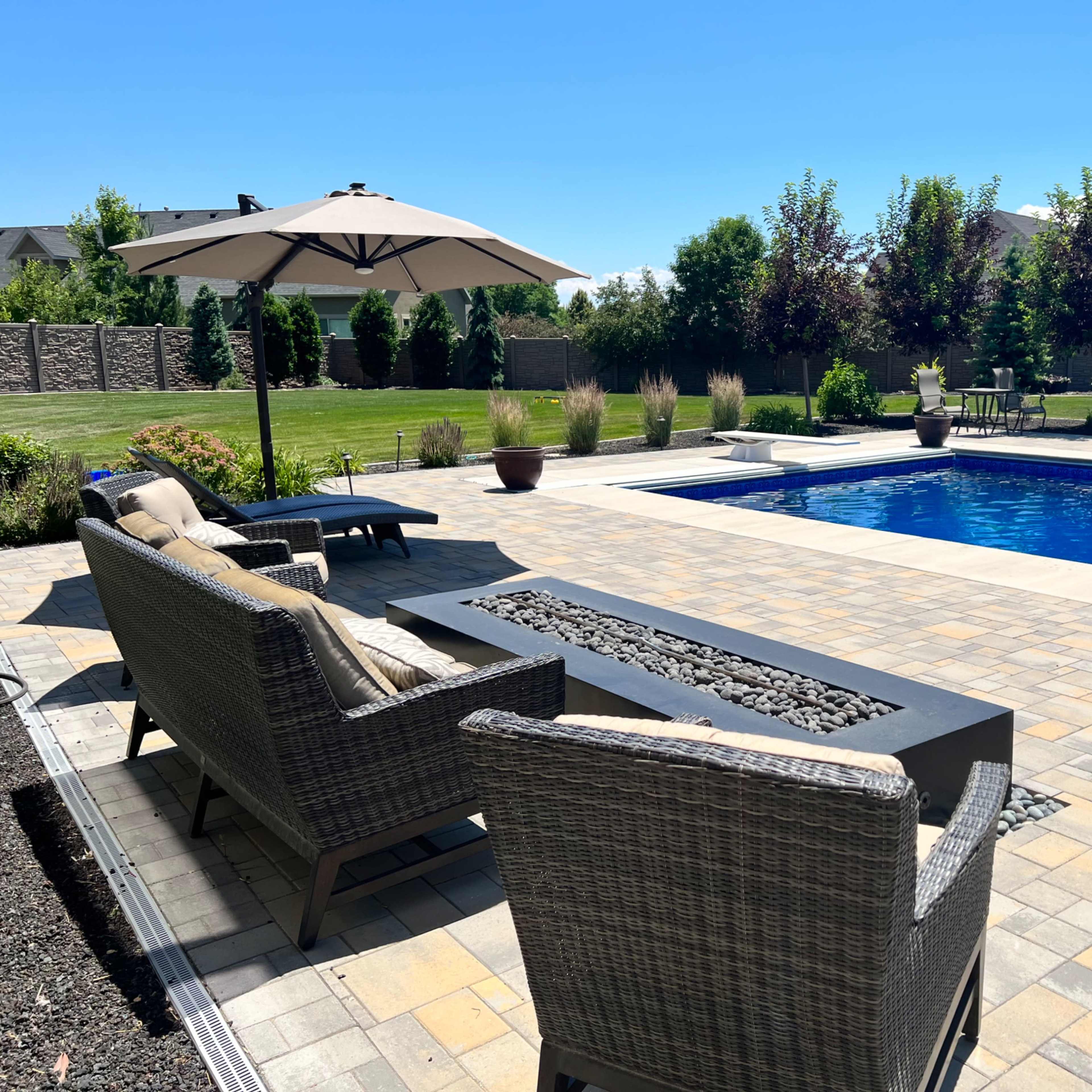 A patio area with two chairs and a table overlooks a blue swimming pool surrounded by greenery and landscaping.