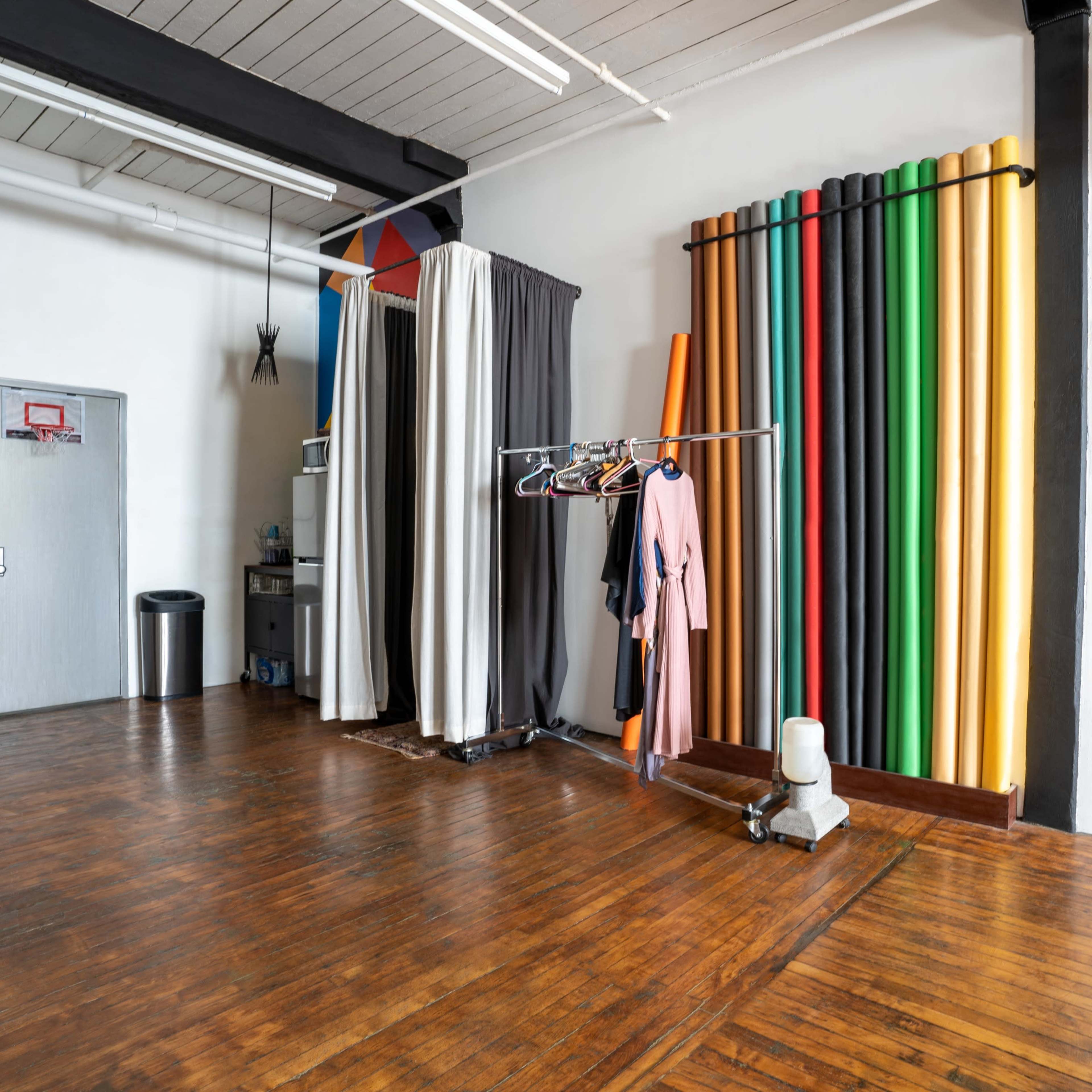 A spacious studio with wooden floors, colorful paper backdrops arranged vertically along a wall, and a clothing rack holding garments.
