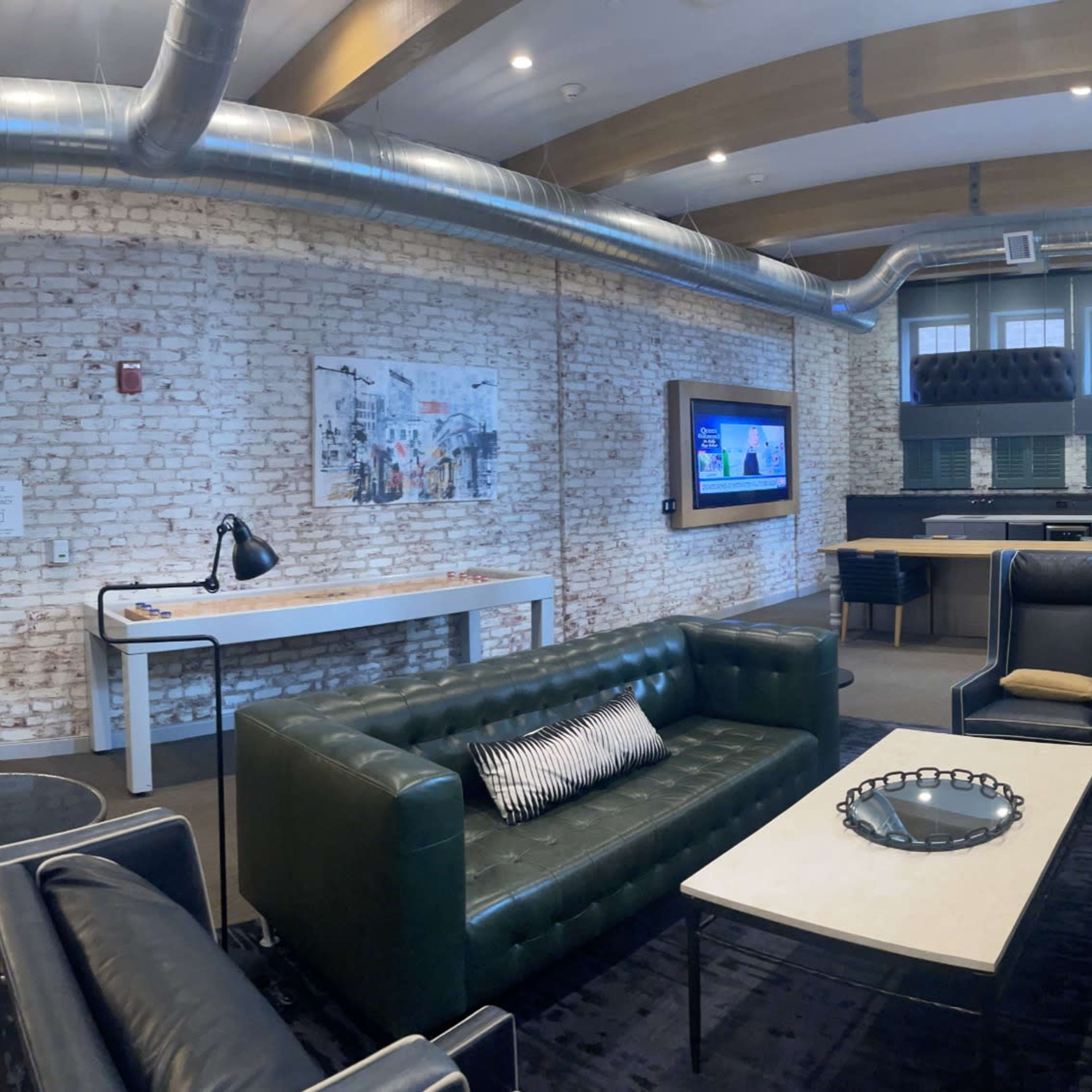 A modern office space featuring exposed brick walls, comfortable seating areas, and a conference room visible through glass doors.