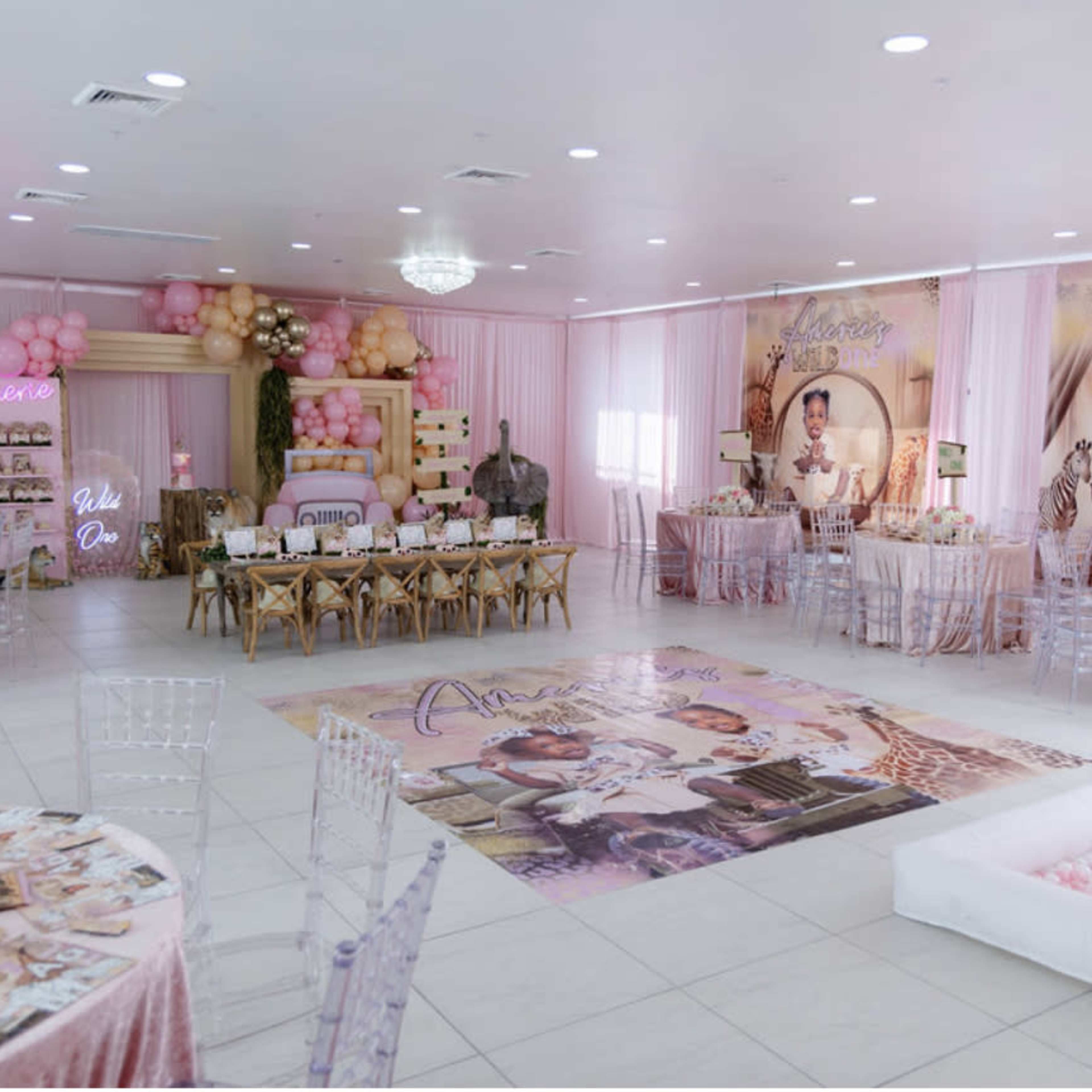 A beautifully decorated event space with pink balloon arrangements, themed table settings, and large photo displays celebrating a special occasion.