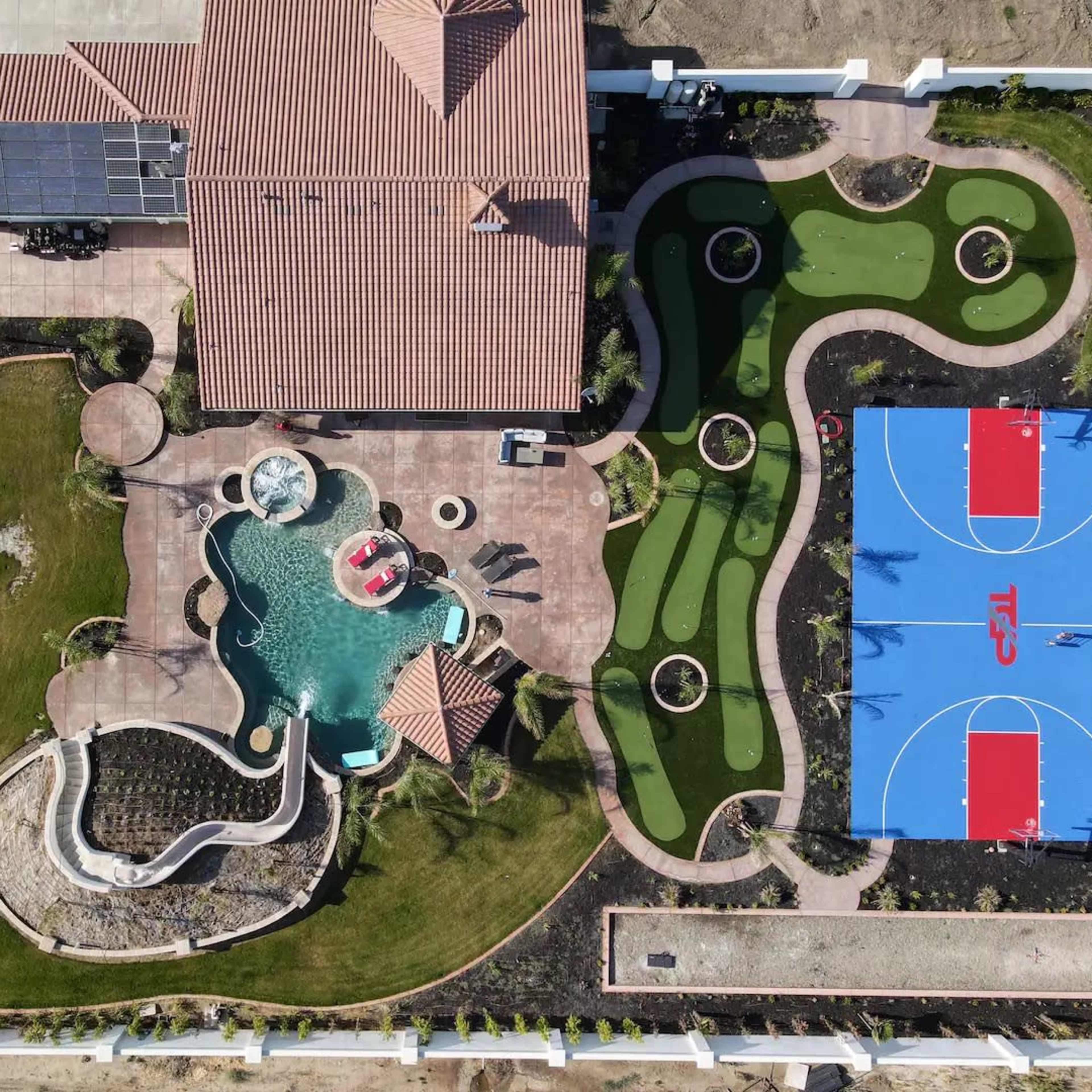 The aerial view shows a residential property featuring a swimming pool, landscaped areas, and two basketball courts.