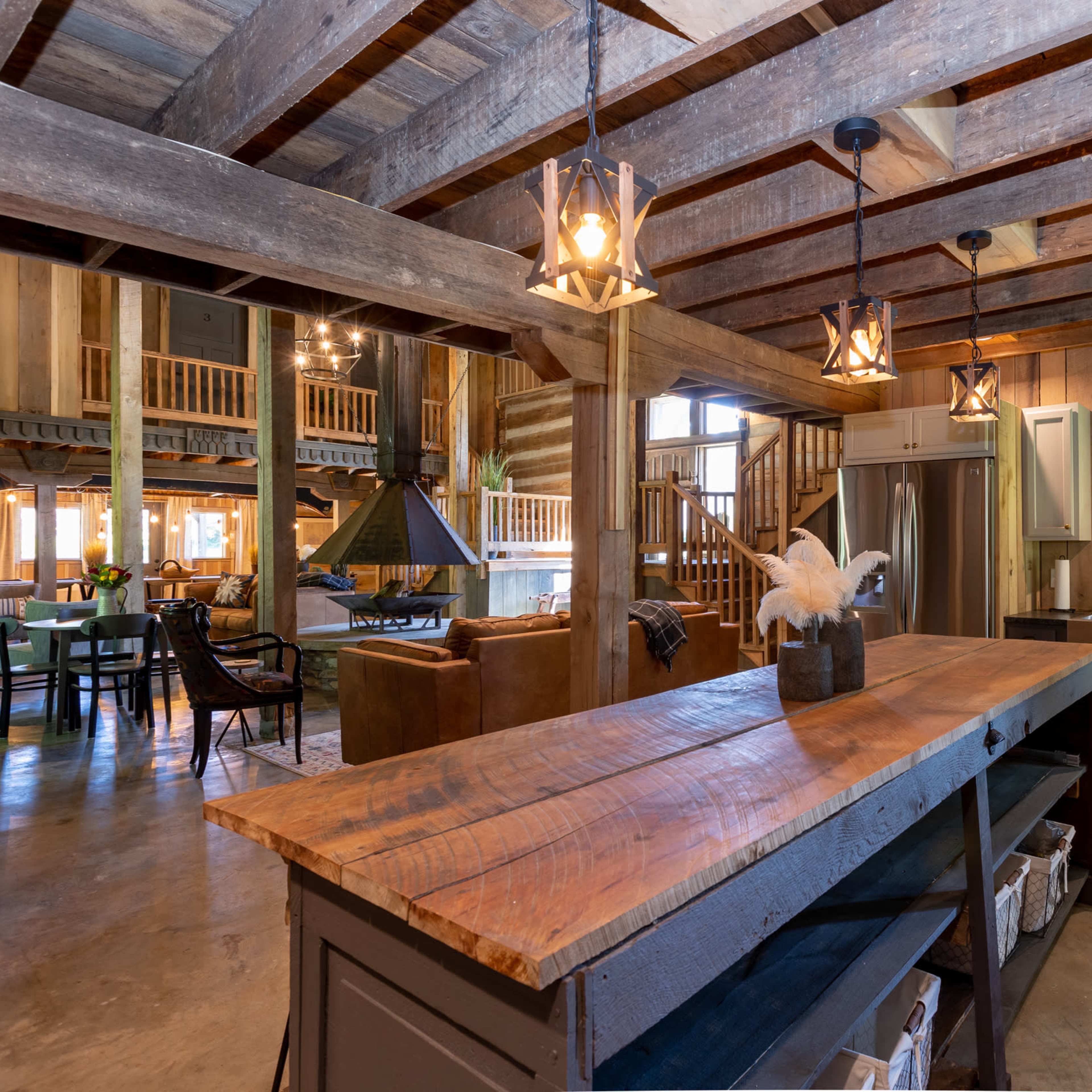 The interior of a rustic kitchen features wooden beams, a large island with a wooden countertop, and modern appliances set against a backdrop of warm wood paneling.