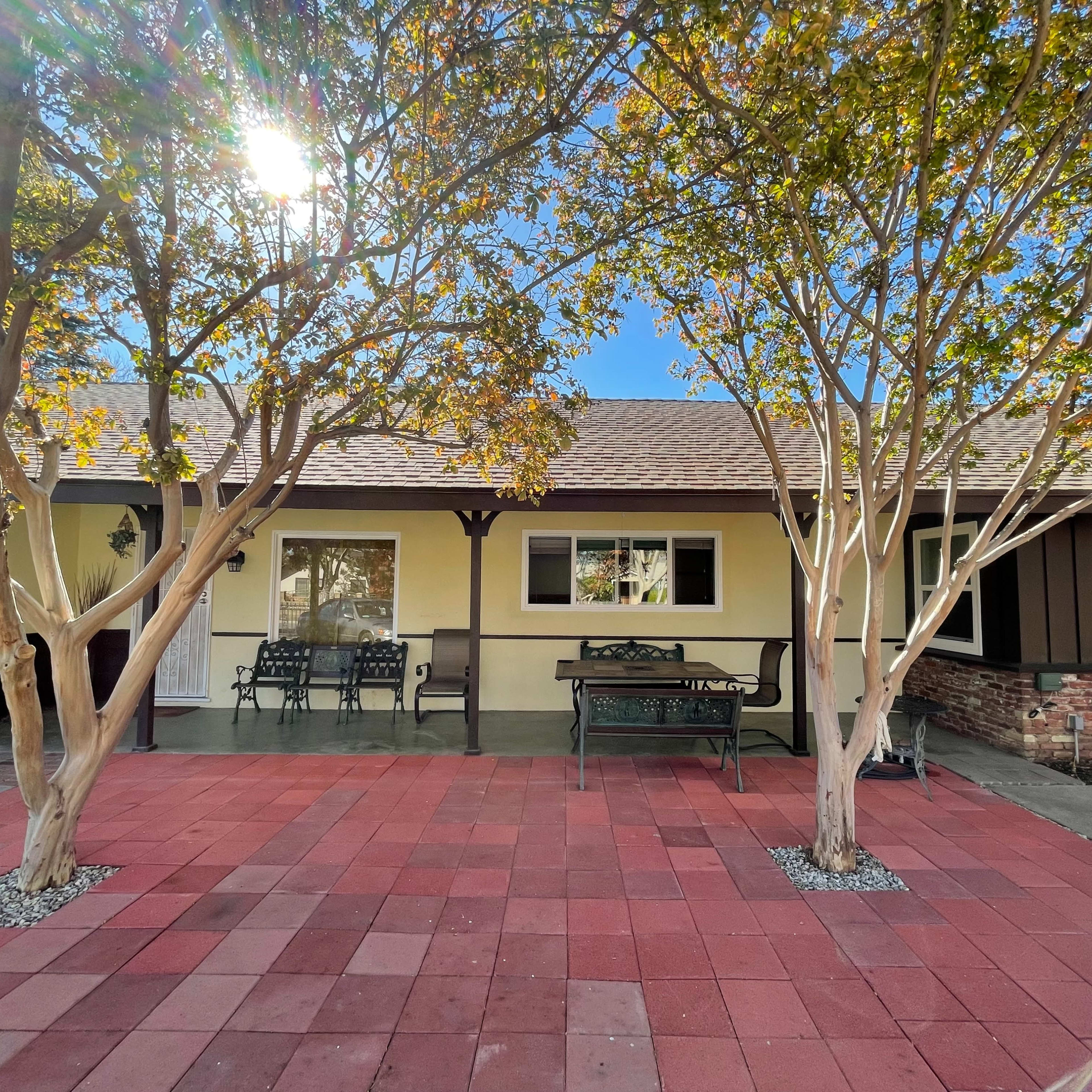 A single-story house with a front porch, flanked by two trees, and a red tiled walkway leading to it.