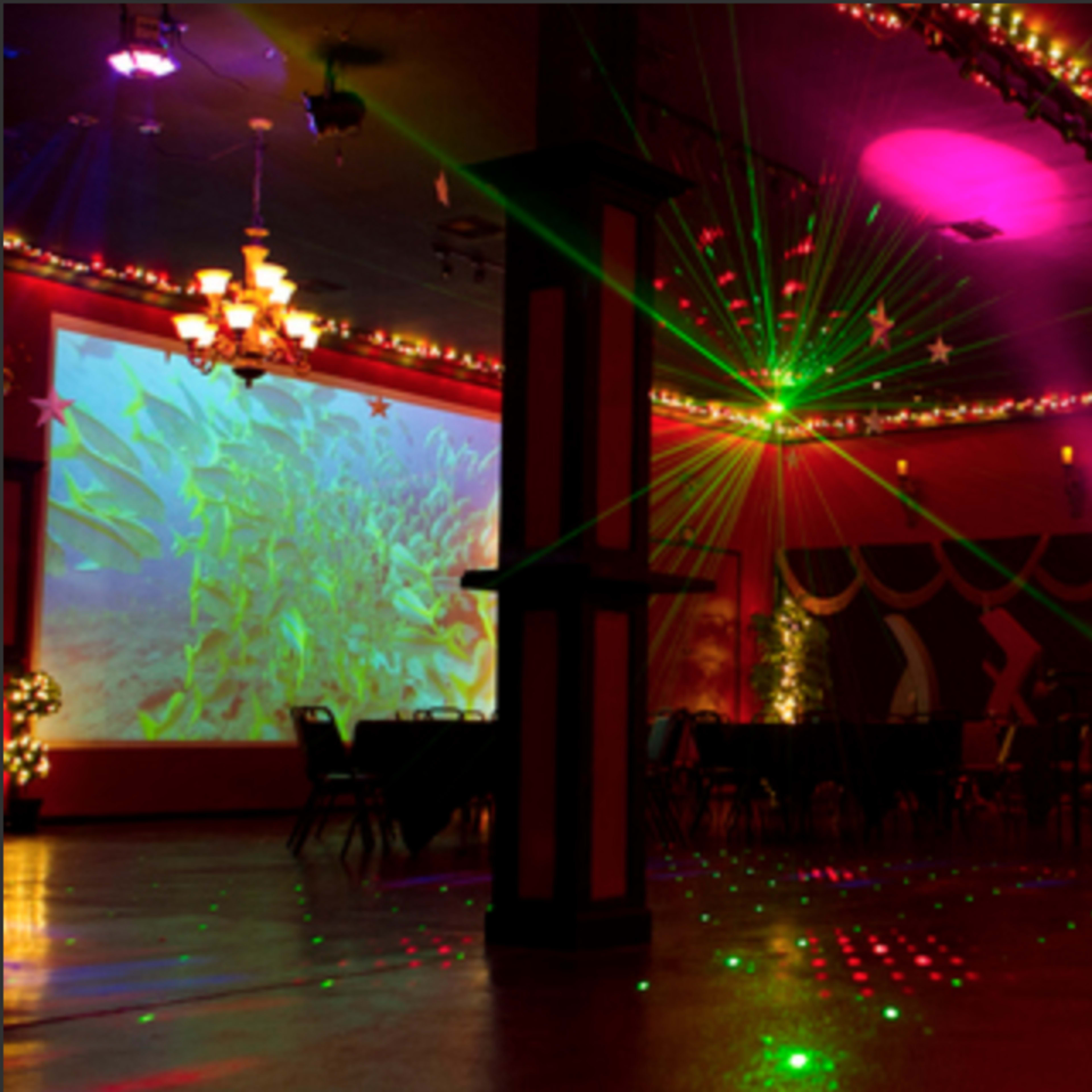 A dimly lit event space decorated with colorful lights, projections on the walls, and tables arranged for a gathering.
