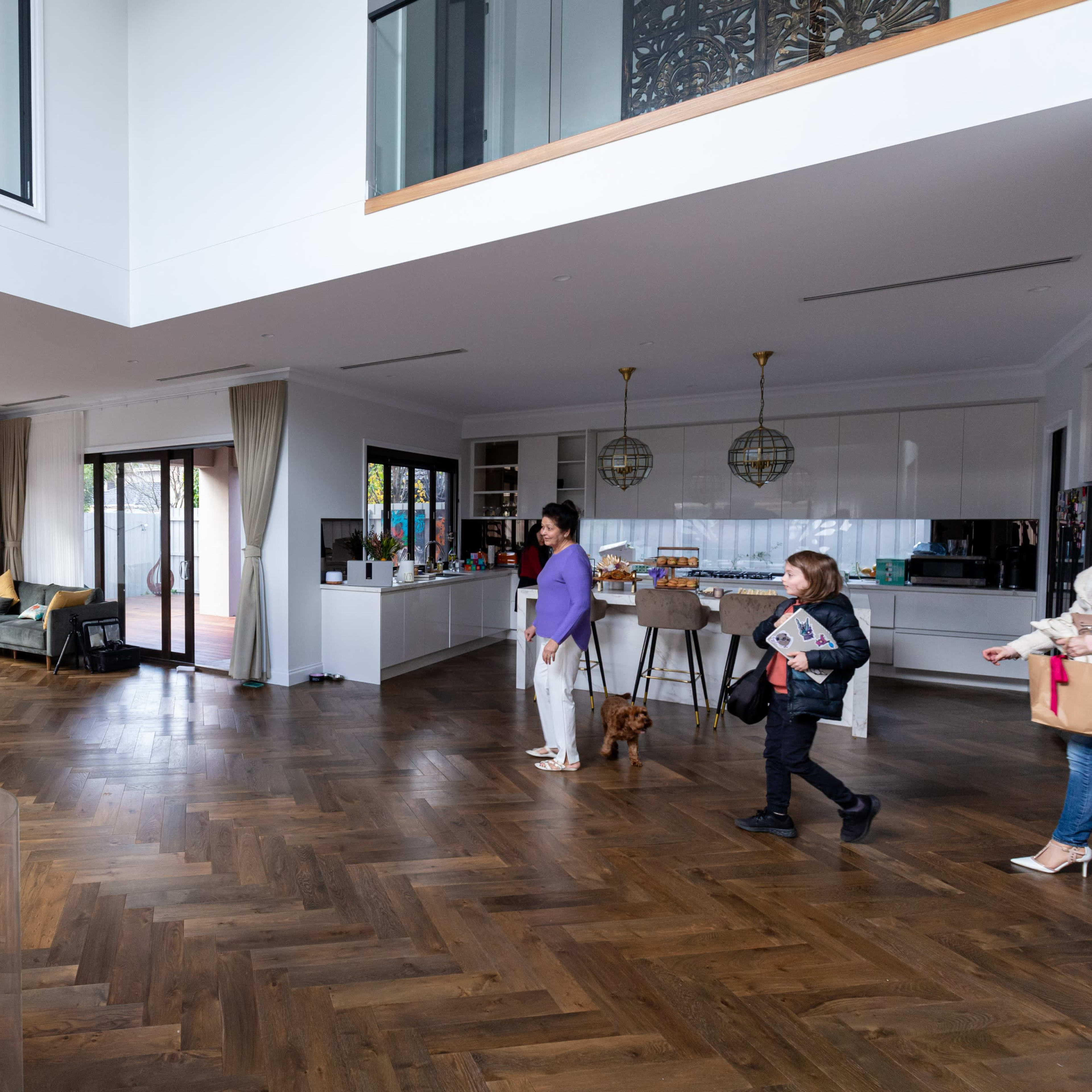 A spacious modern interior with wooden flooring, a balloon arch, guests mingling, and a bar area in the background.