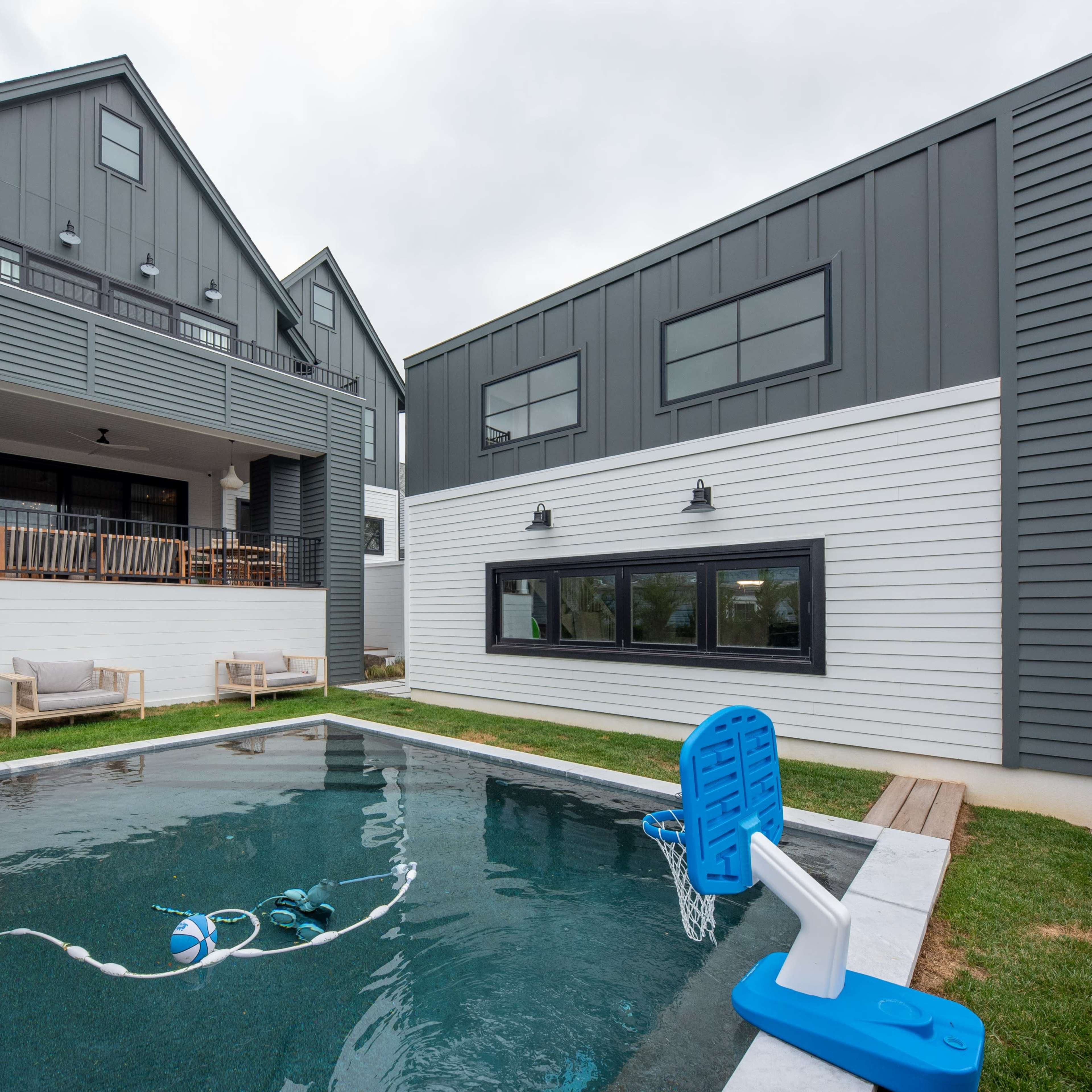 A modern house with a gray exterior, featuring a swimming pool in the backyard and a basketball hoop attached to the pool edge.