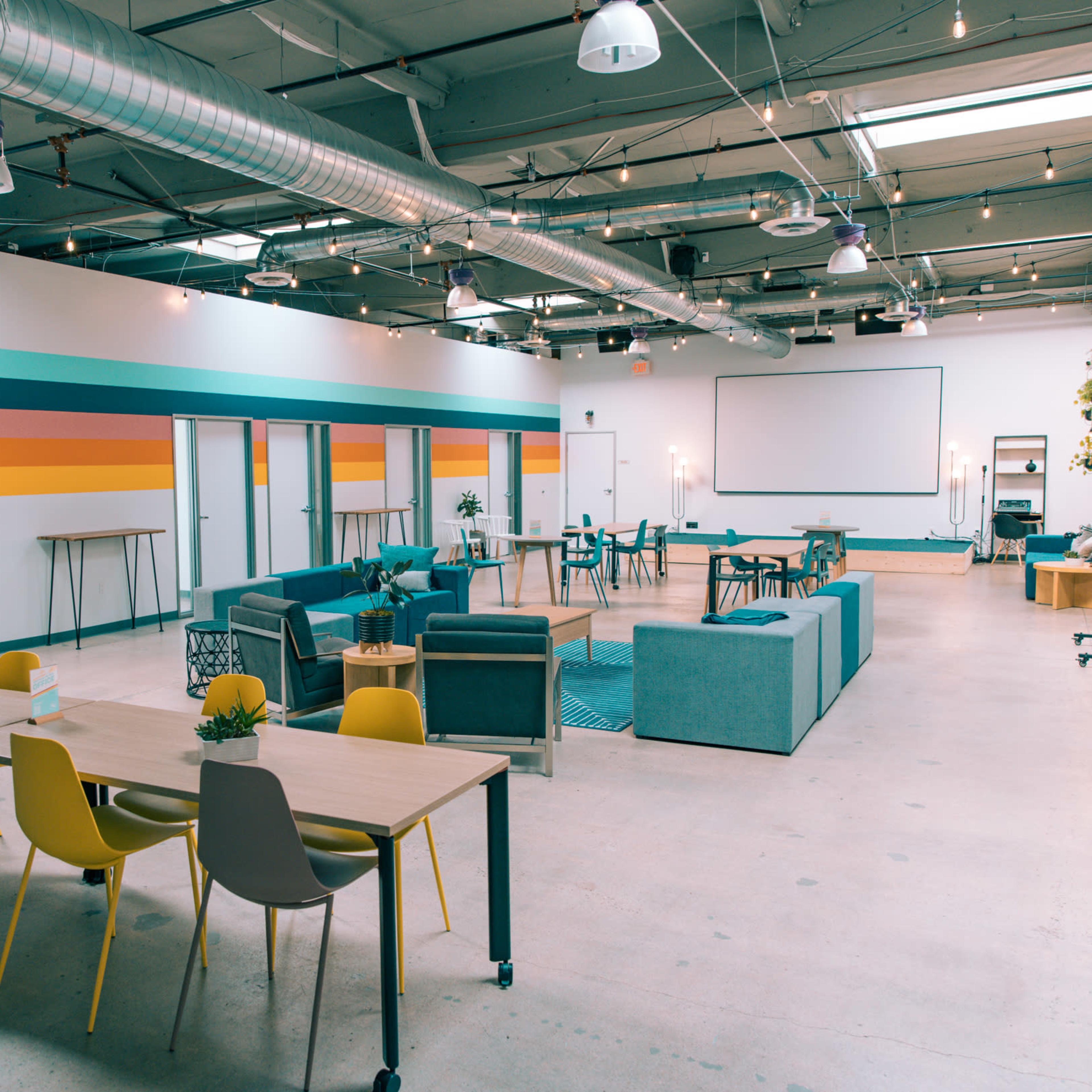 A spacious, modern meeting area with colorful accent walls, various seating arrangements, and tables for collaboration.