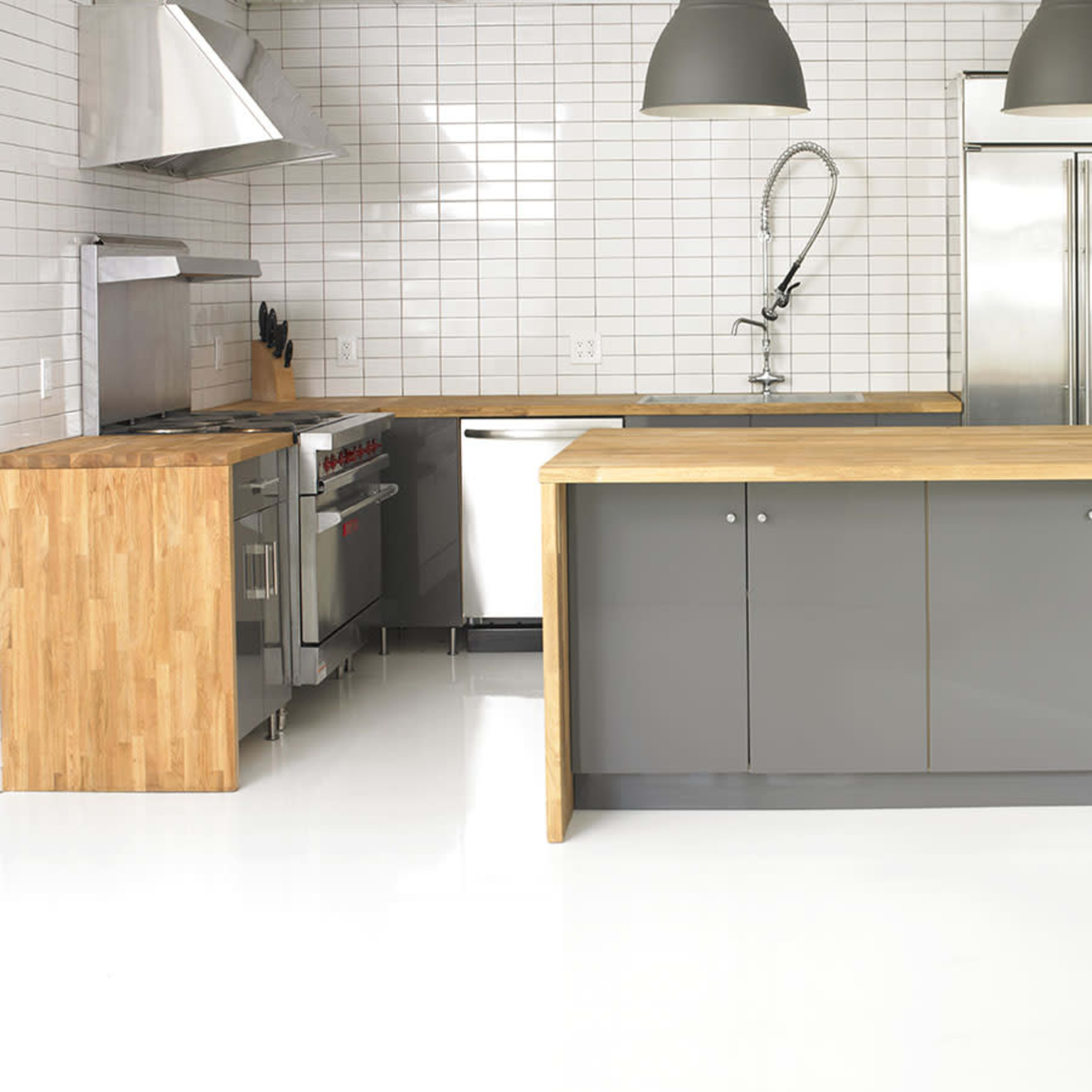 A modern kitchen featuring a central wooden island, stainless steel appliances, and a tiled backsplash.