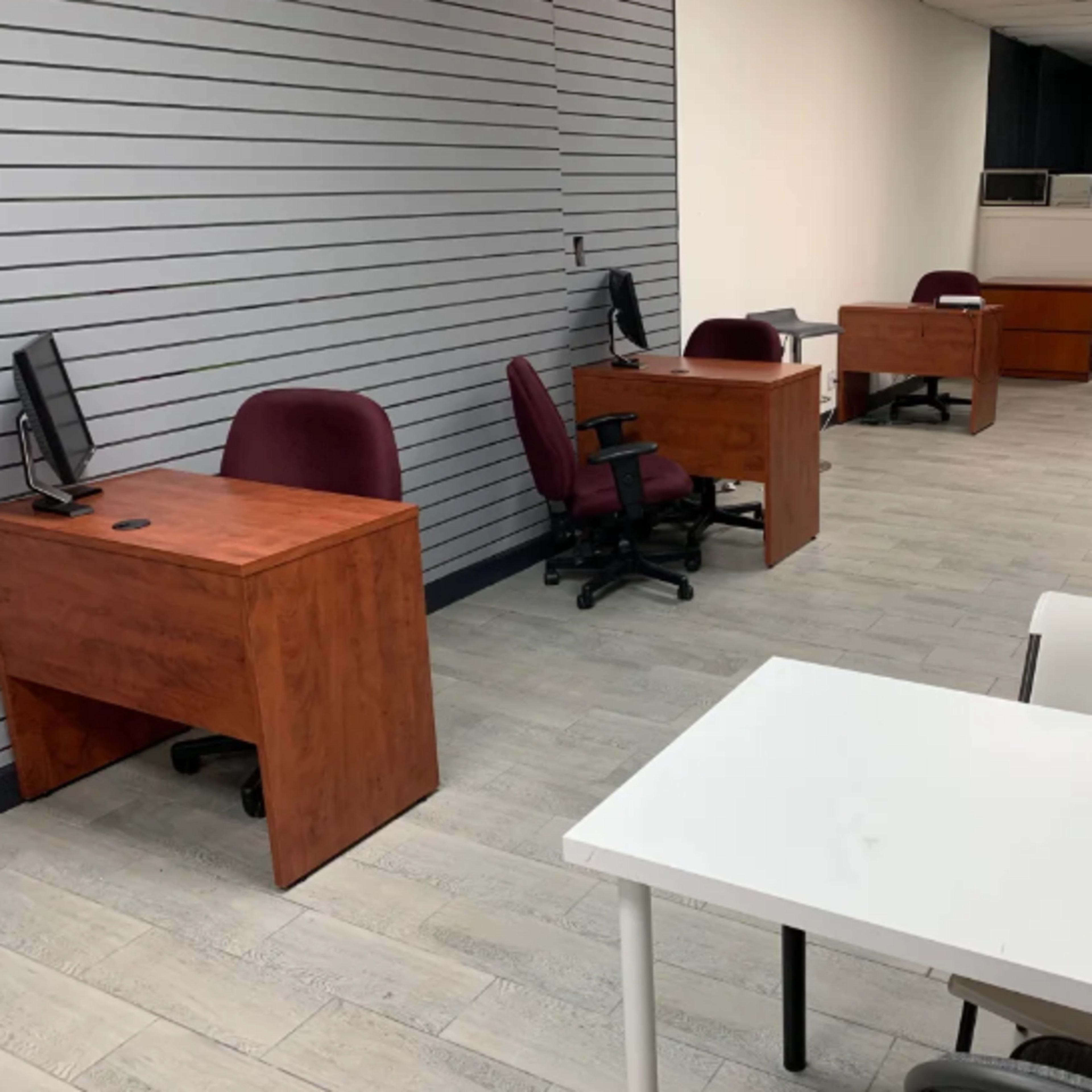 A spacious office interior with several wooden desks, ergonomic chairs, and minimalist decor.