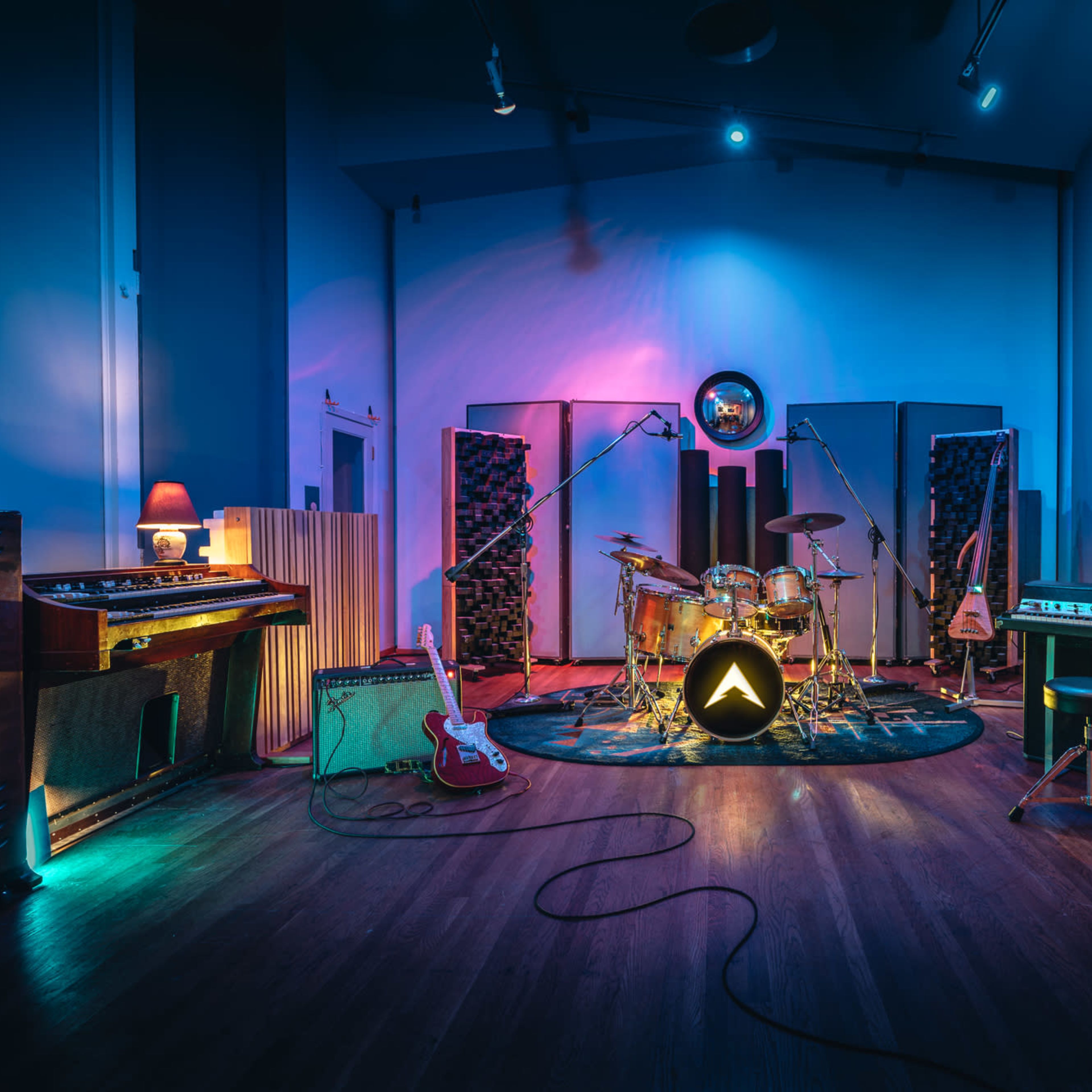 A well-equipped music studio featuring a drum set, guitars, keyboards, and audio equipment surrounded by sound-absorbing panels and colorful lighting.