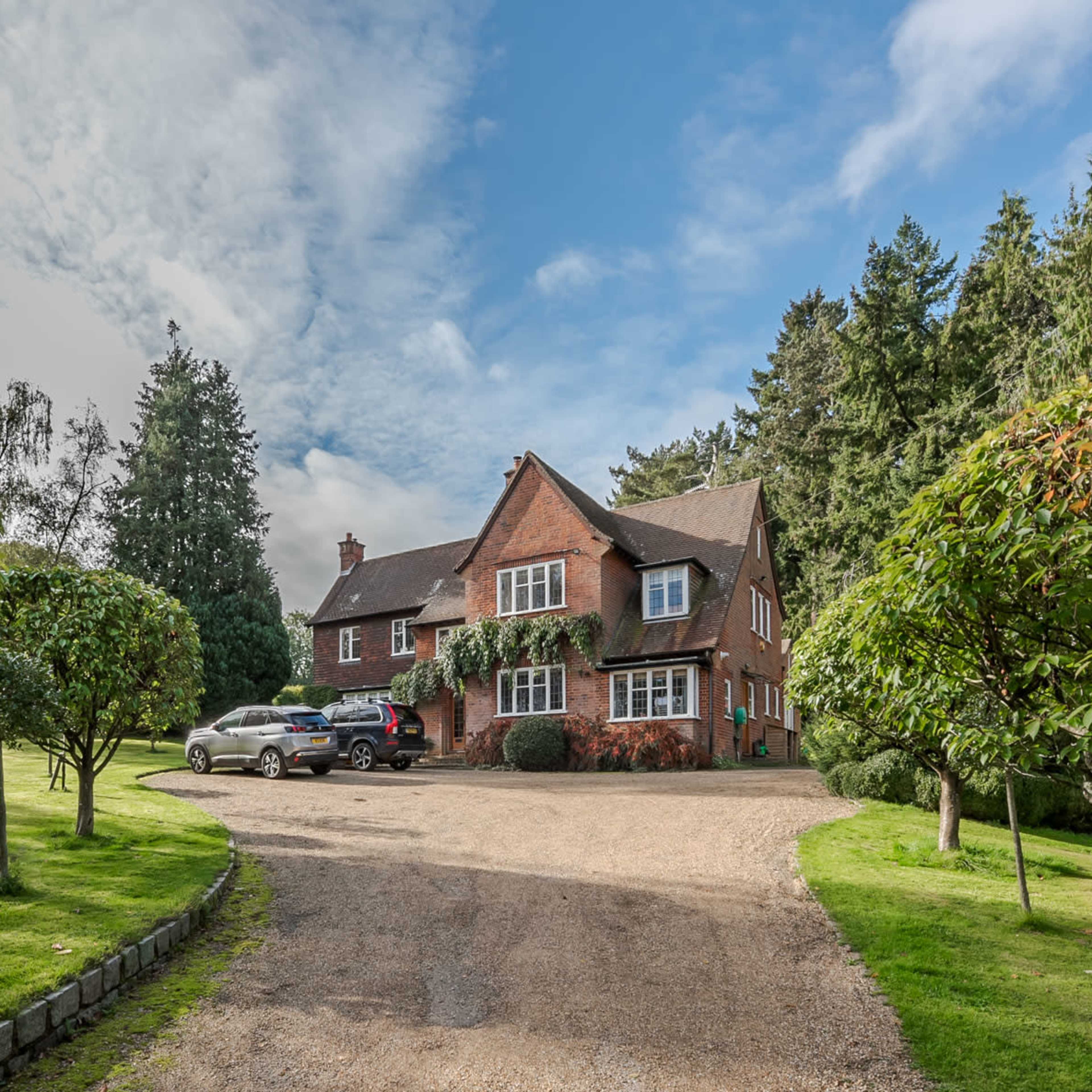 A spacious brick house is set alongside a gravel driveway, surrounded by neatly trimmed grass and trees.