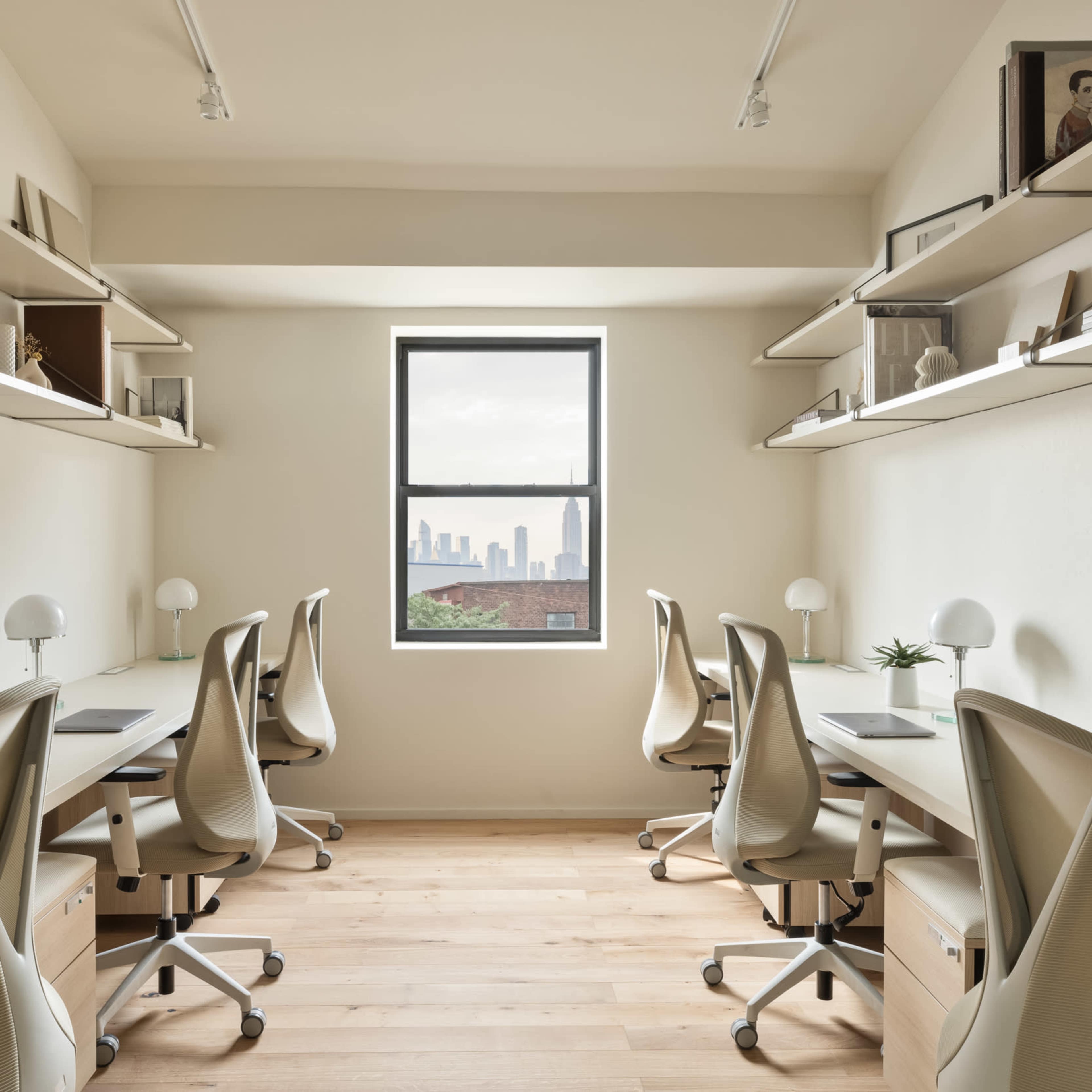 A bright, minimalist office space with five workstations featuring ergonomic chairs and shelves filled with books and decor, all arranged along the walls.