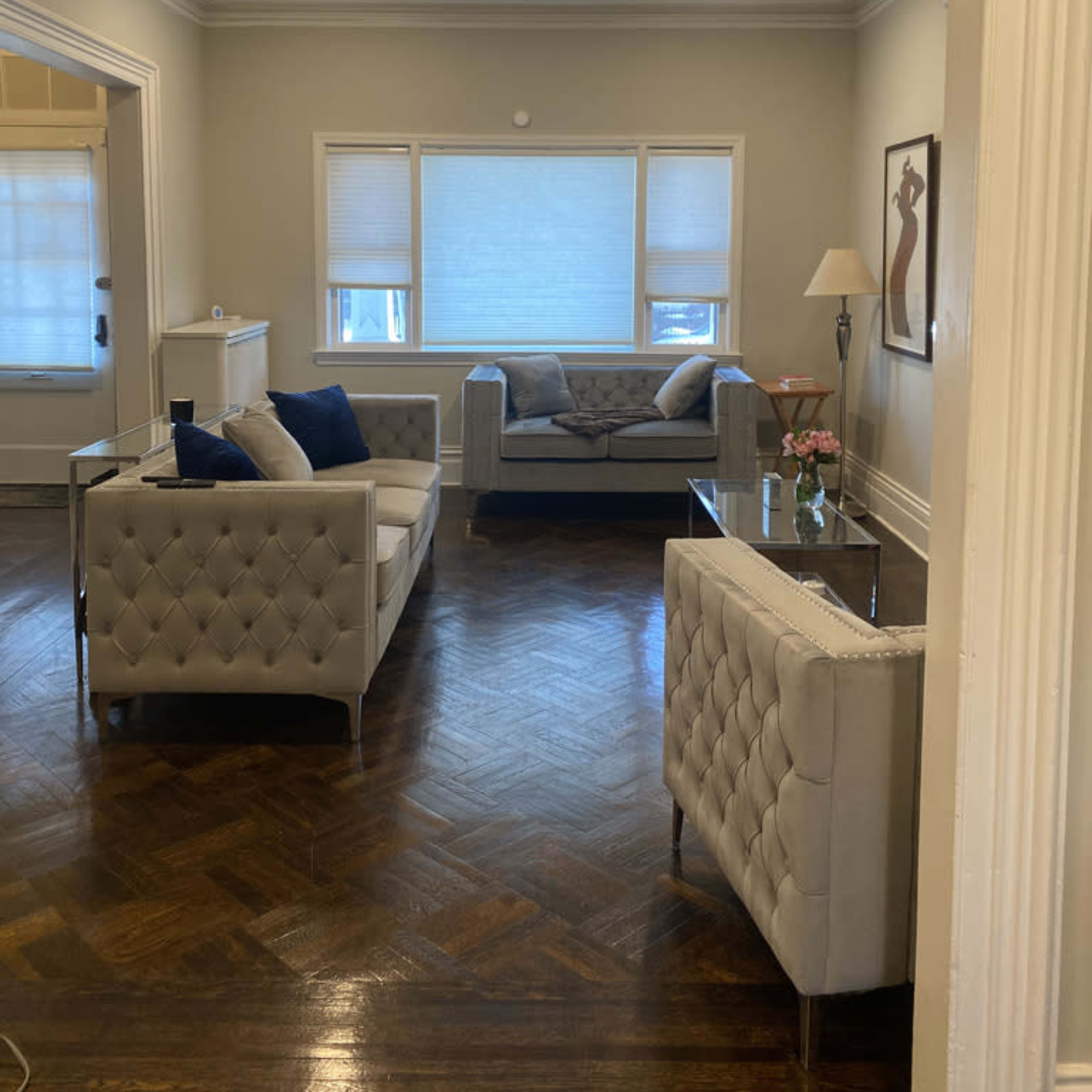 A well-lit living room with two matching sofas, a glass coffee table, and a lamp beside a large window.
