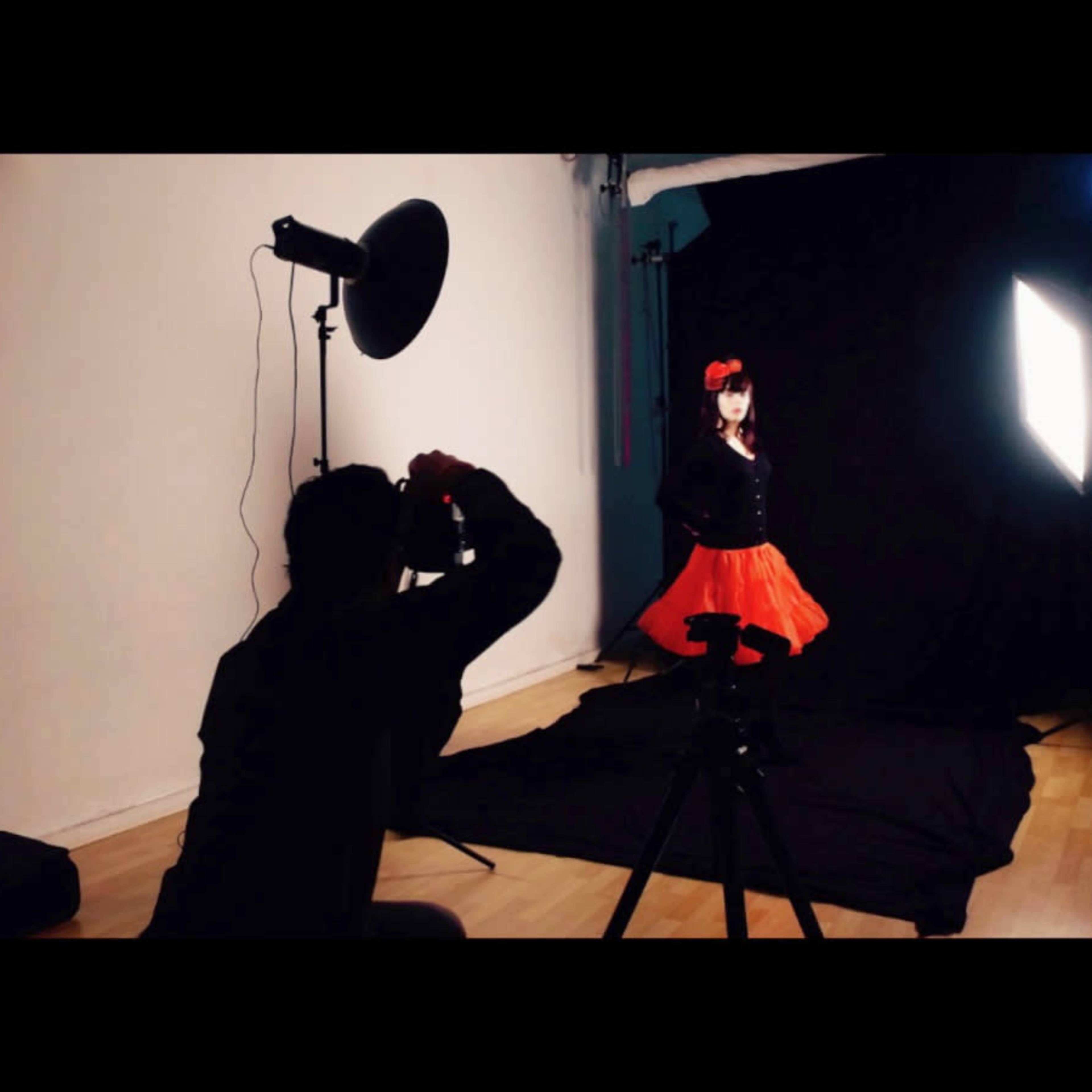 A photographer captures a portrait of a child in a red dress against a black backdrop in a studio setting.