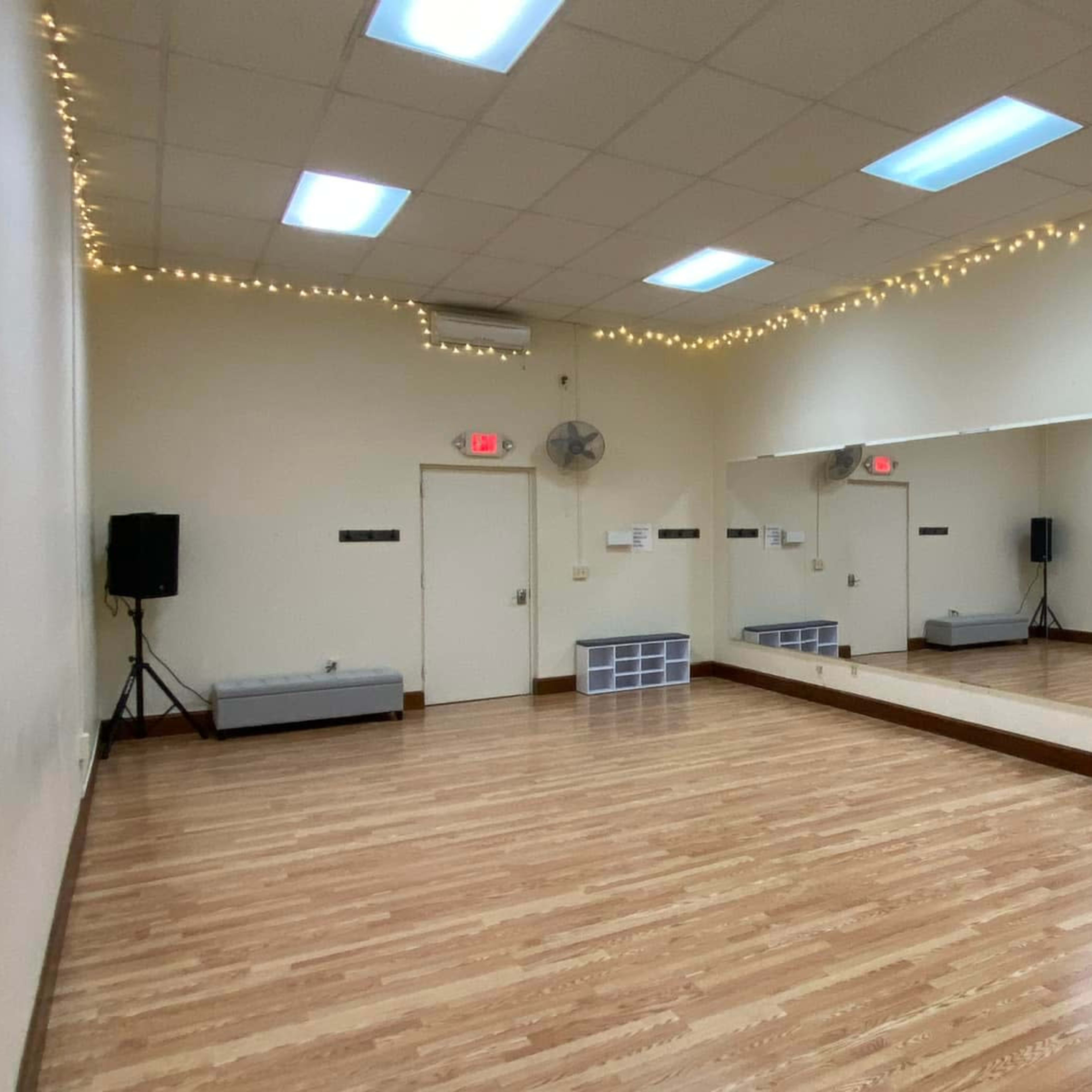 A dance studio with wooden flooring, wall mirrors, and soft lighting along the ceiling.
