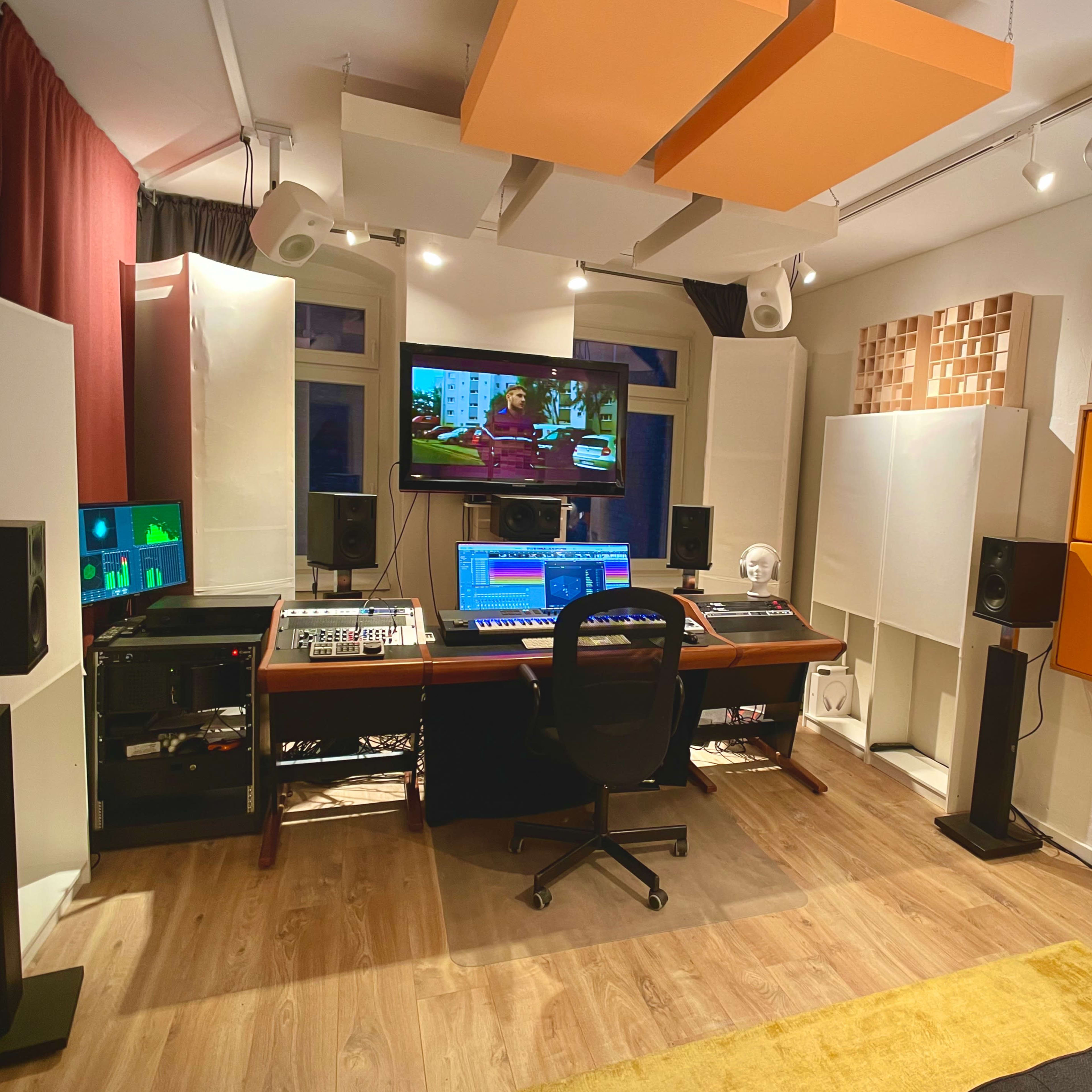 A modern recording studio with a computer workstation, speakers, and soundproofing panels.