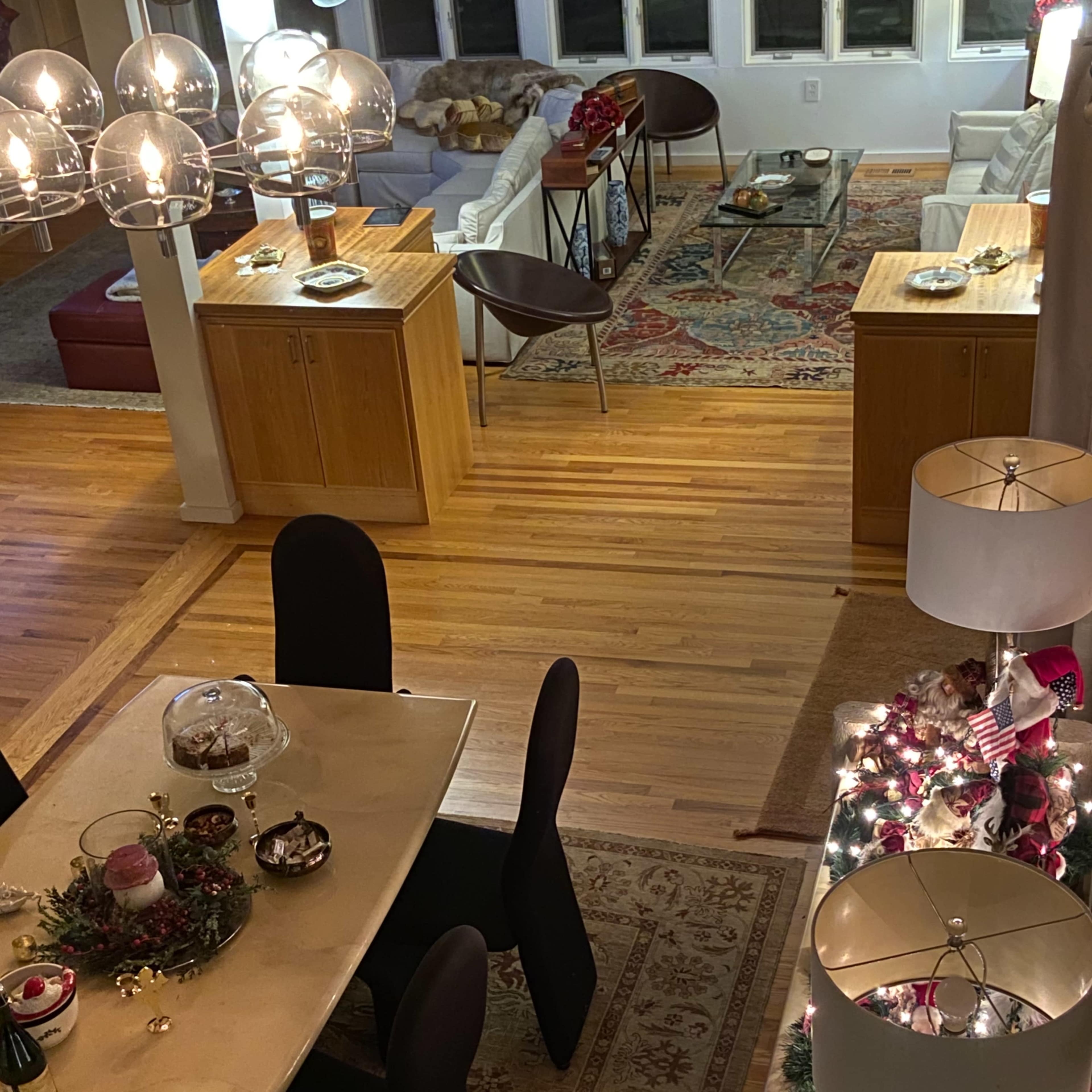 A well-lit dining area with a long table set for a meal and a cozy living room in the background featuring a sectional sofa and decorative accents.