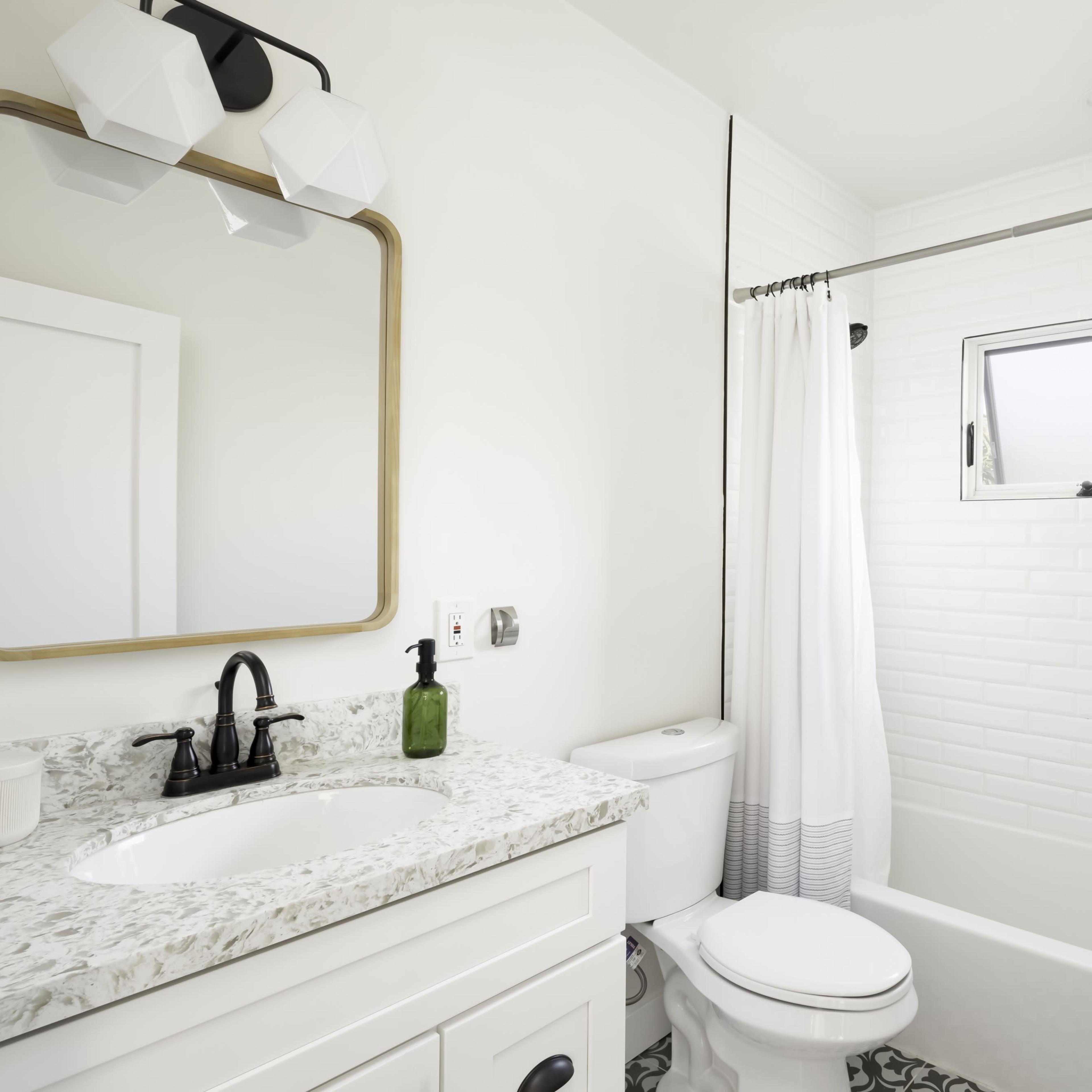 A modern bathroom featuring a white tile wall, a bathtub with a shower curtain, a marble countertop sink, and a mirror above it.