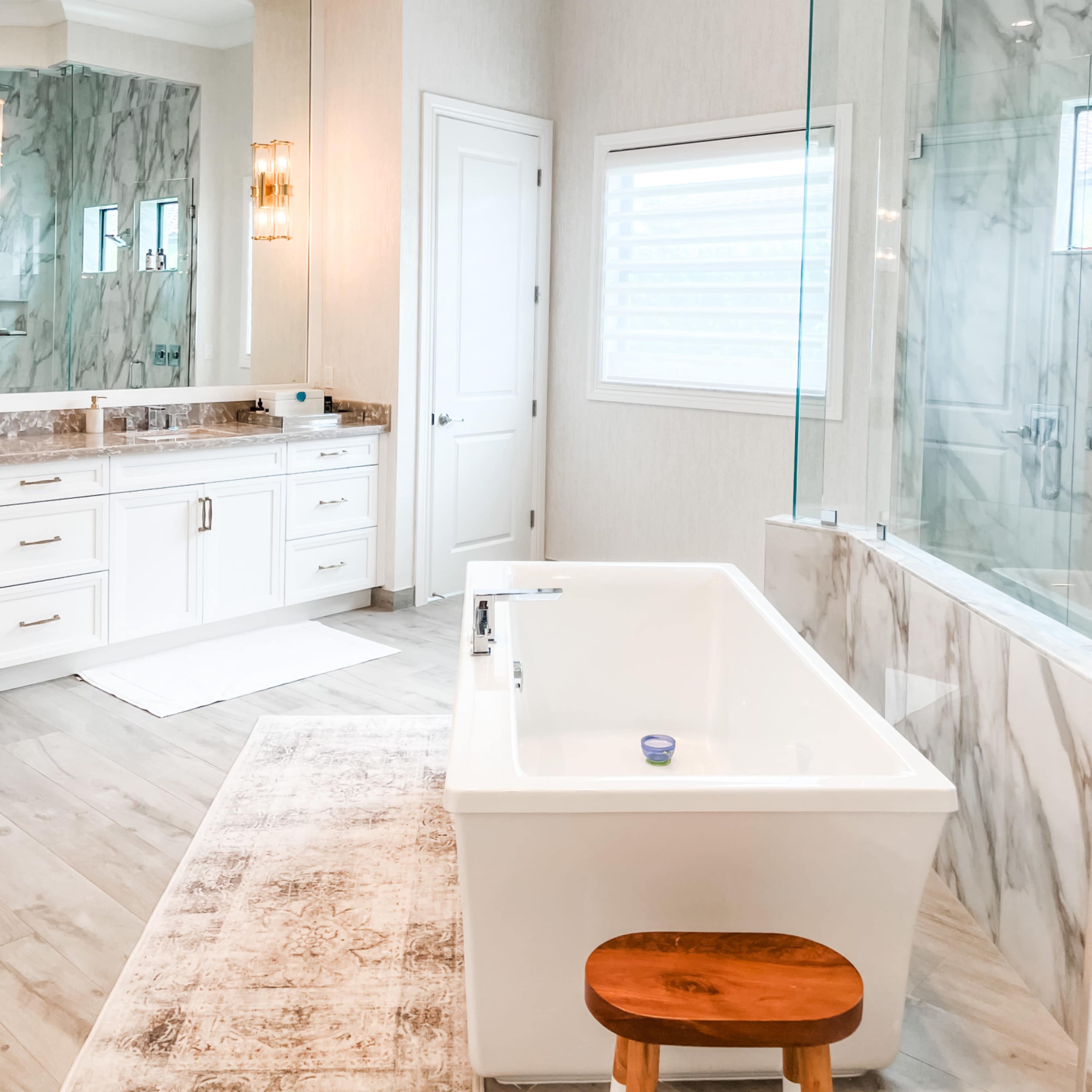 A well-lit bathroom features a freestanding bathtub, a large mirrored vanity, and a glass-enclosed shower.