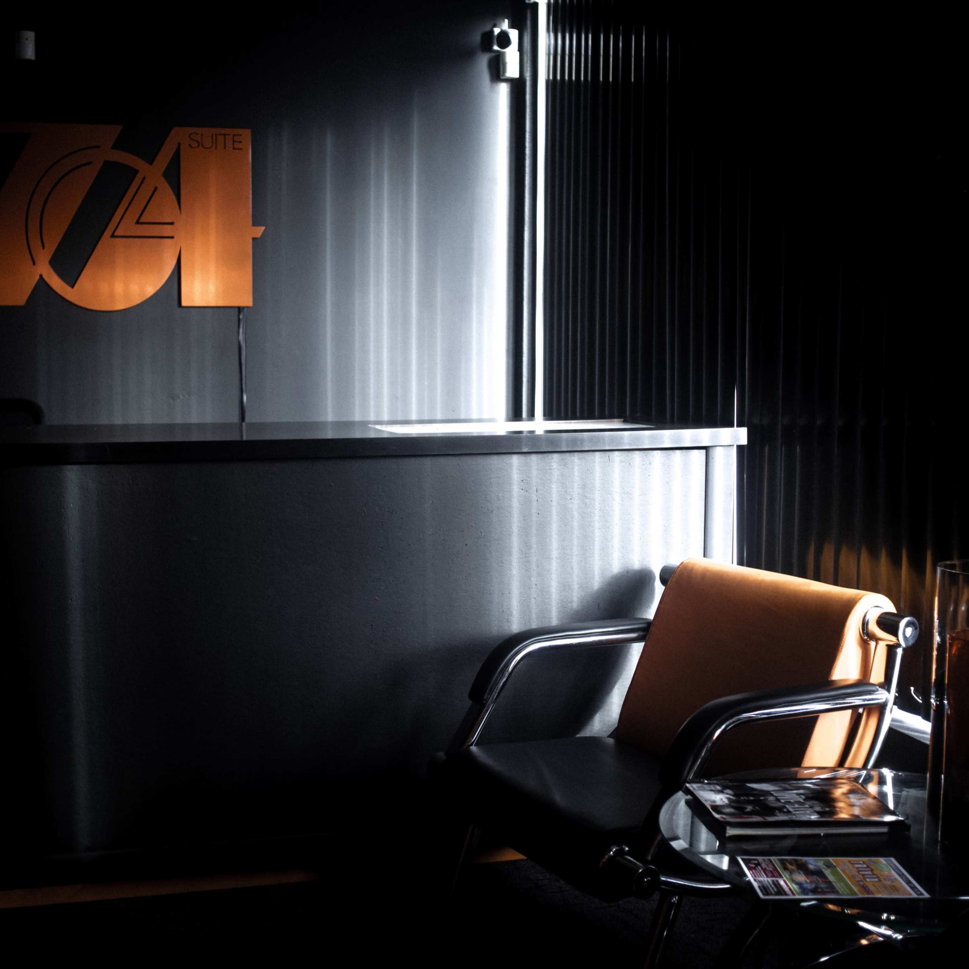 A modern reception area features a sleek metallic counter with a large "704" sign and a chair next to a glass side table.