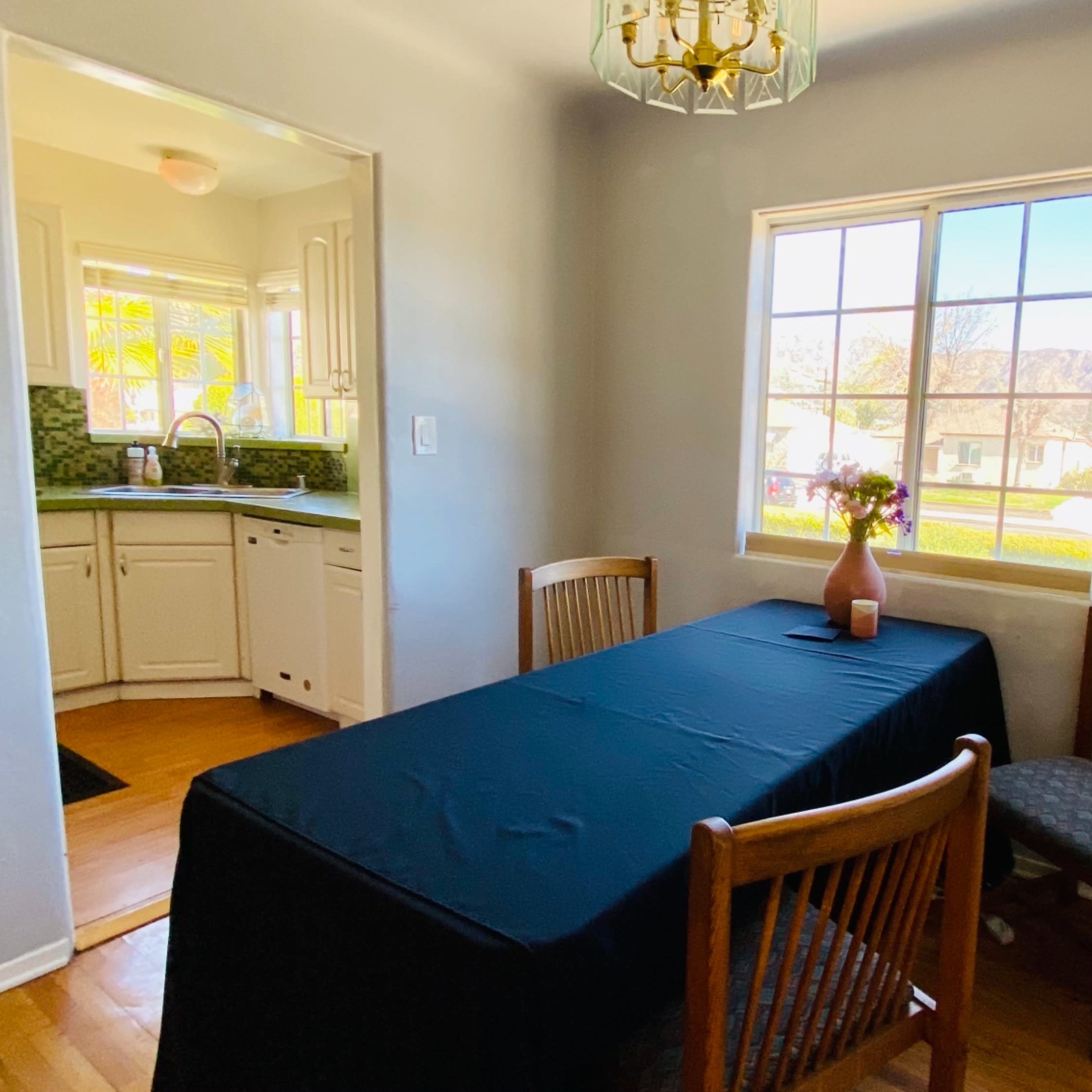 A dining area features a table covered with a black cloth and four wooden chairs, with a window providing natural light and a view of the outdoors.
