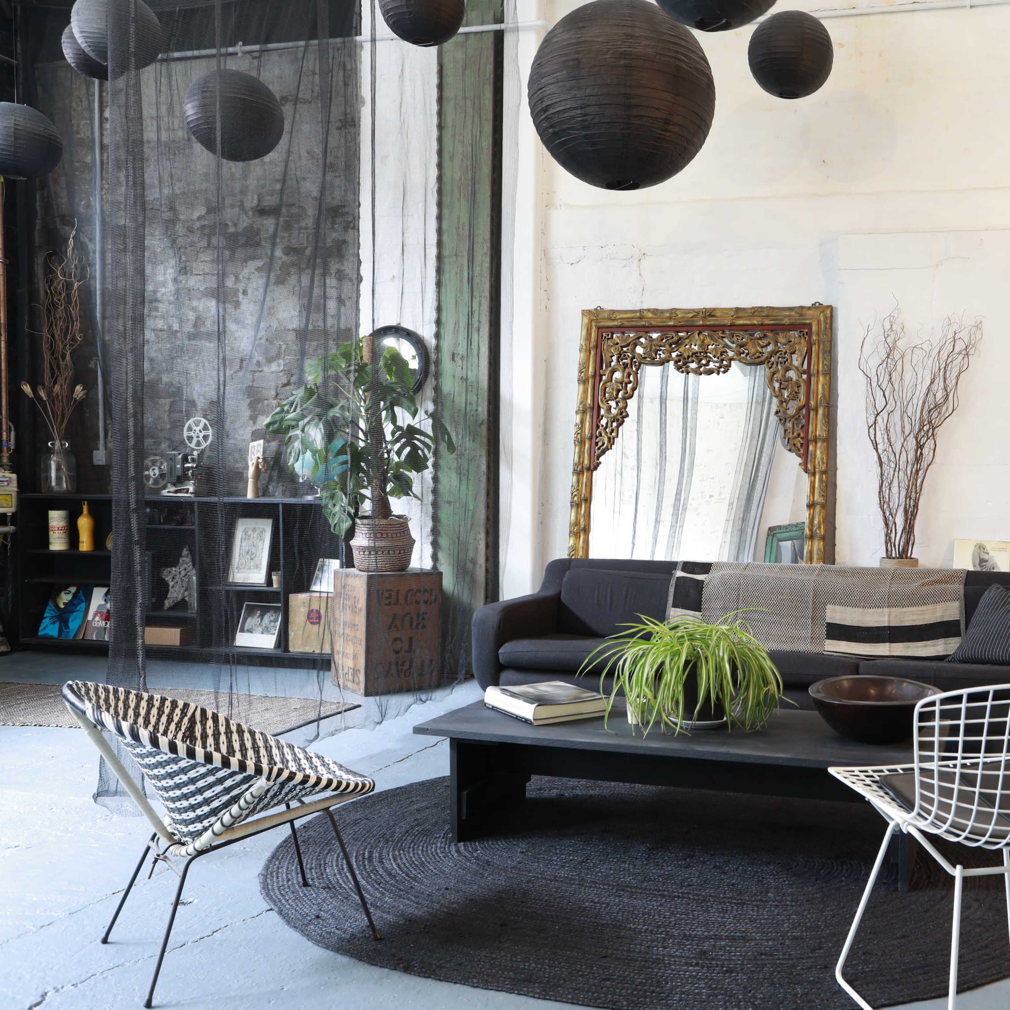 A modern living room with a black sofa, a round coffee table, and decorative elements like hanging lanterns and a large mirror against a white wall.