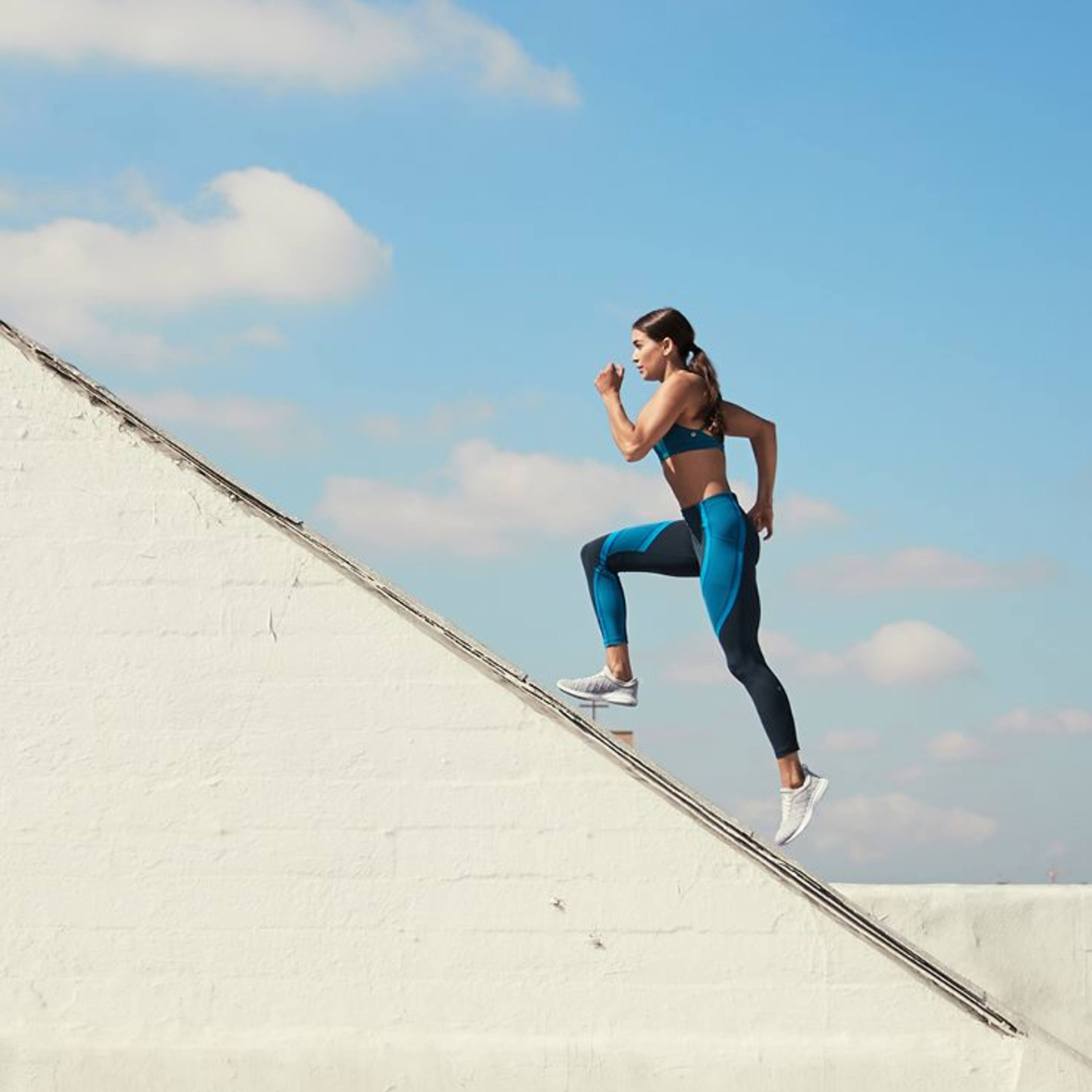 A woman in athletic wear runs up an inclined rooftop against a clear blue sky.