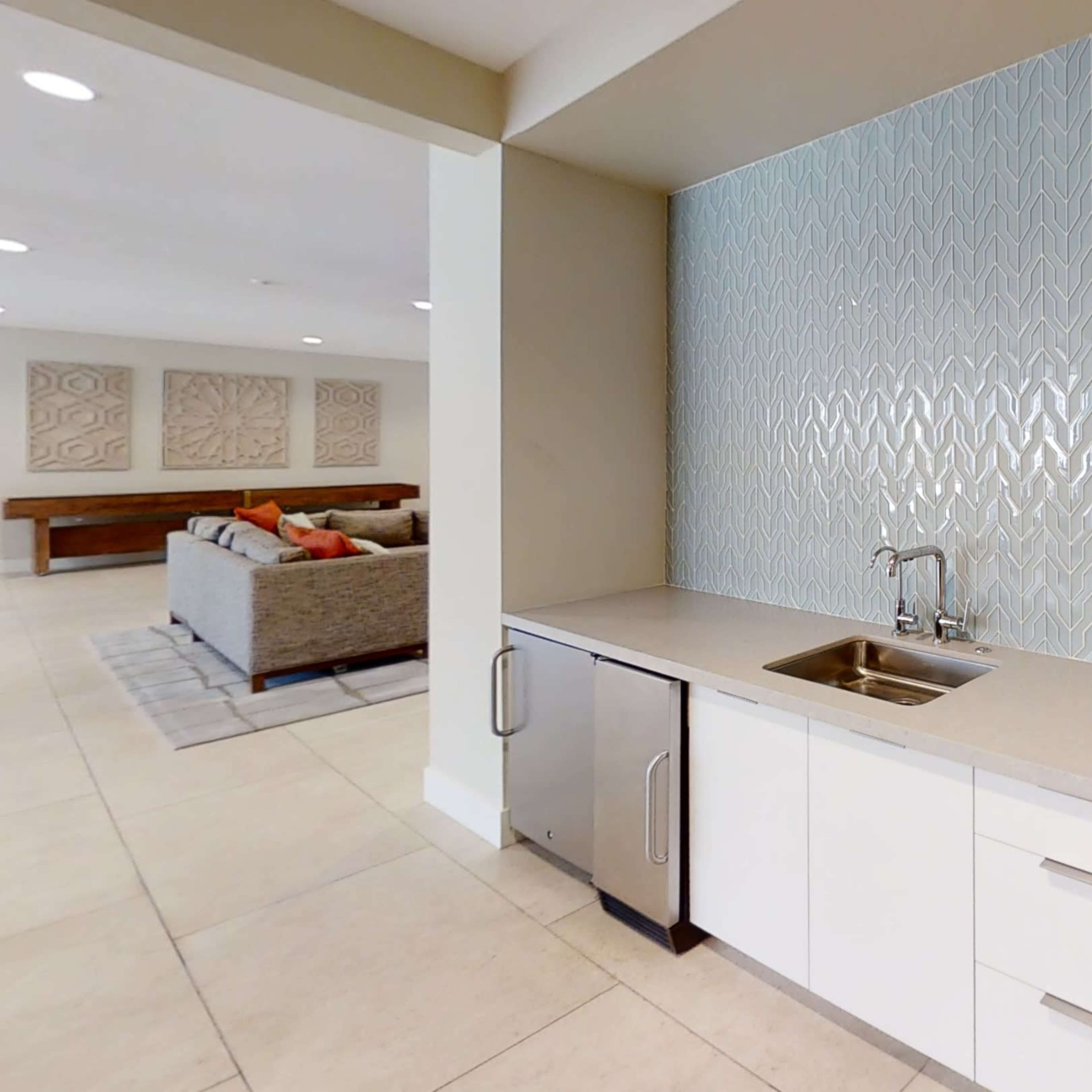 A modern kitchen area with a light-colored countertop, a stainless steel sink, a microwave, and a patterned backsplash.