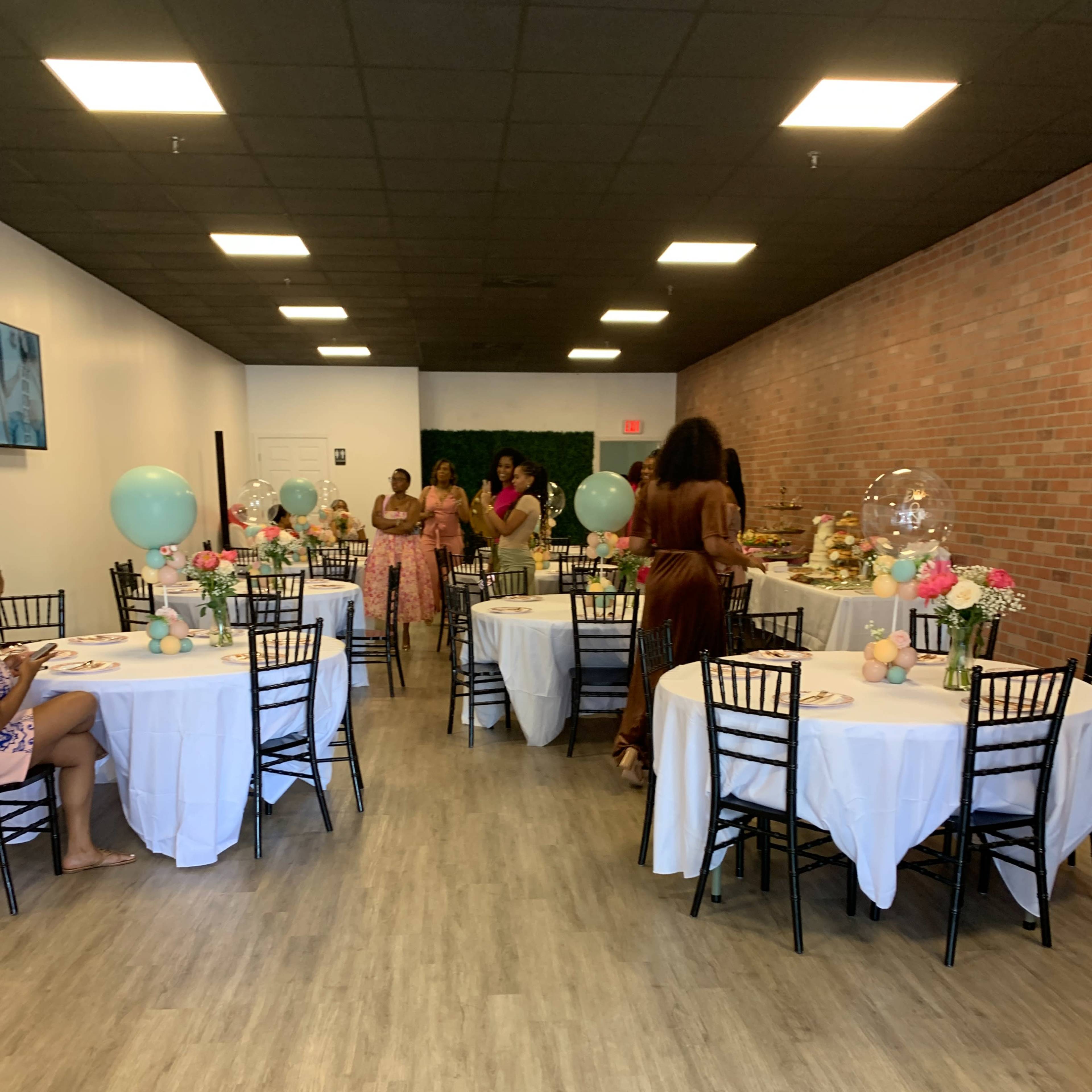 A decorated event space with several tables set for a celebration, featuring floral centerpieces and balloons.