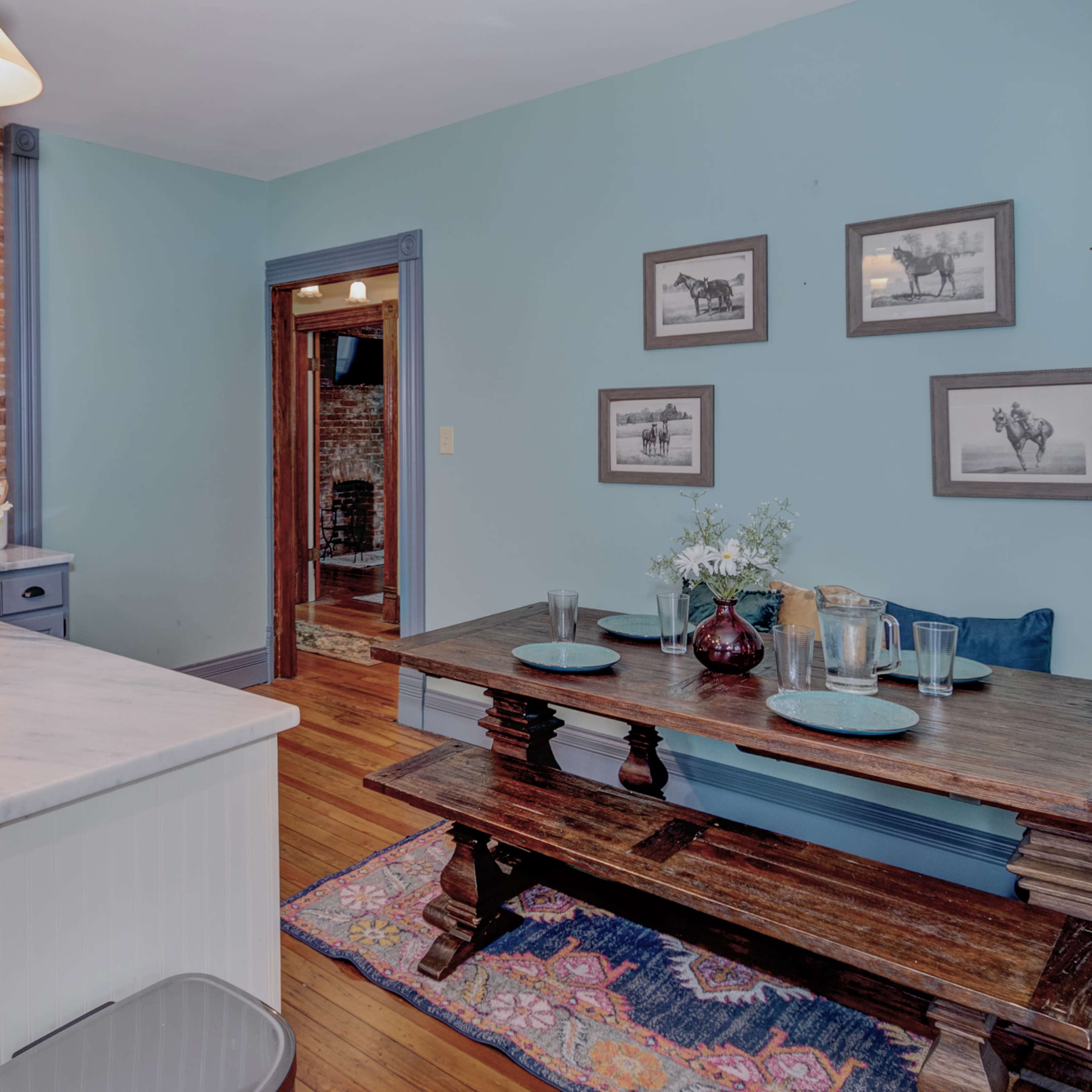 A kitchen and dining area with a wooden dining table, a marble-topped island, and exposed brick walls.