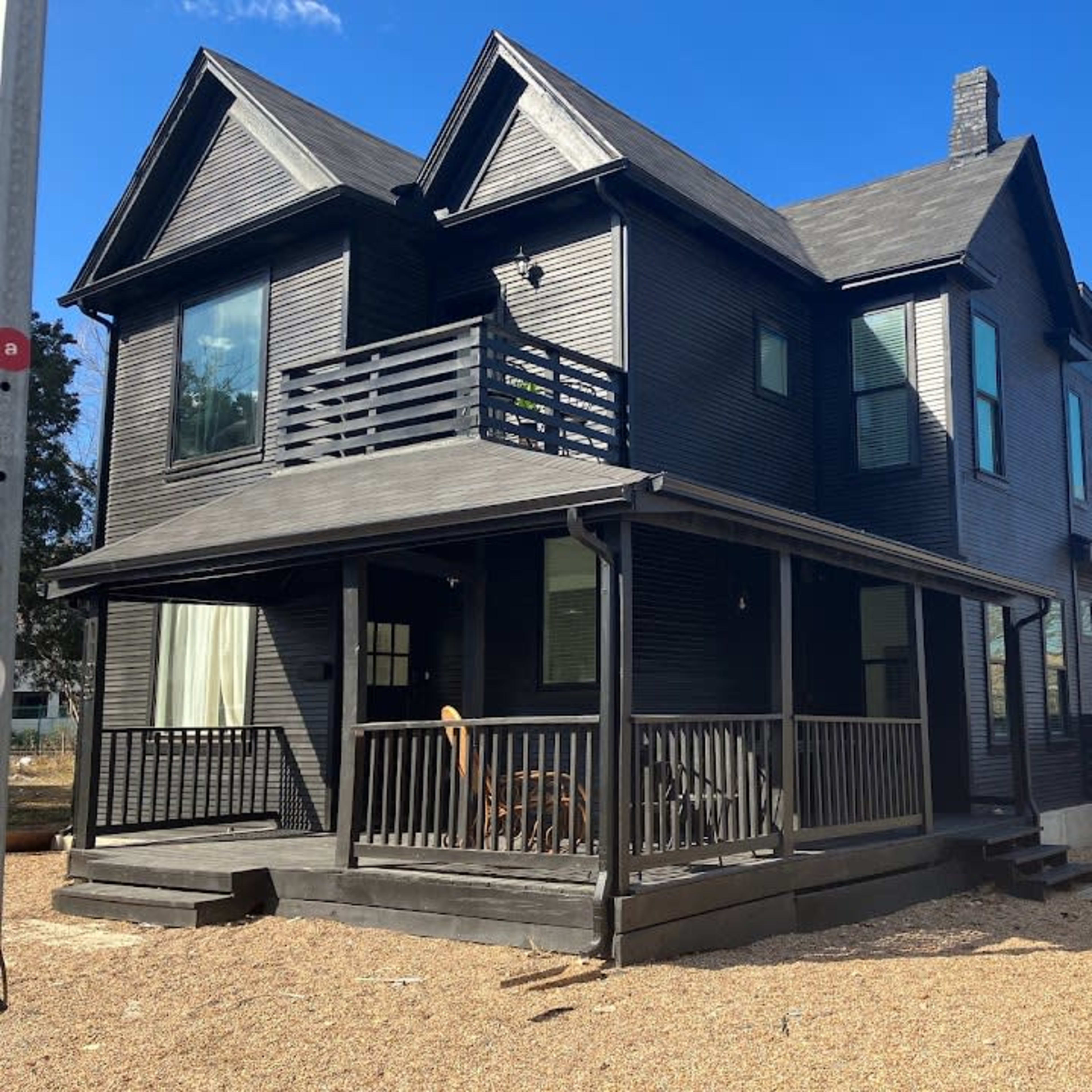 A black-painted two-story house features a porch with a railing and a landscaped gravel yard.