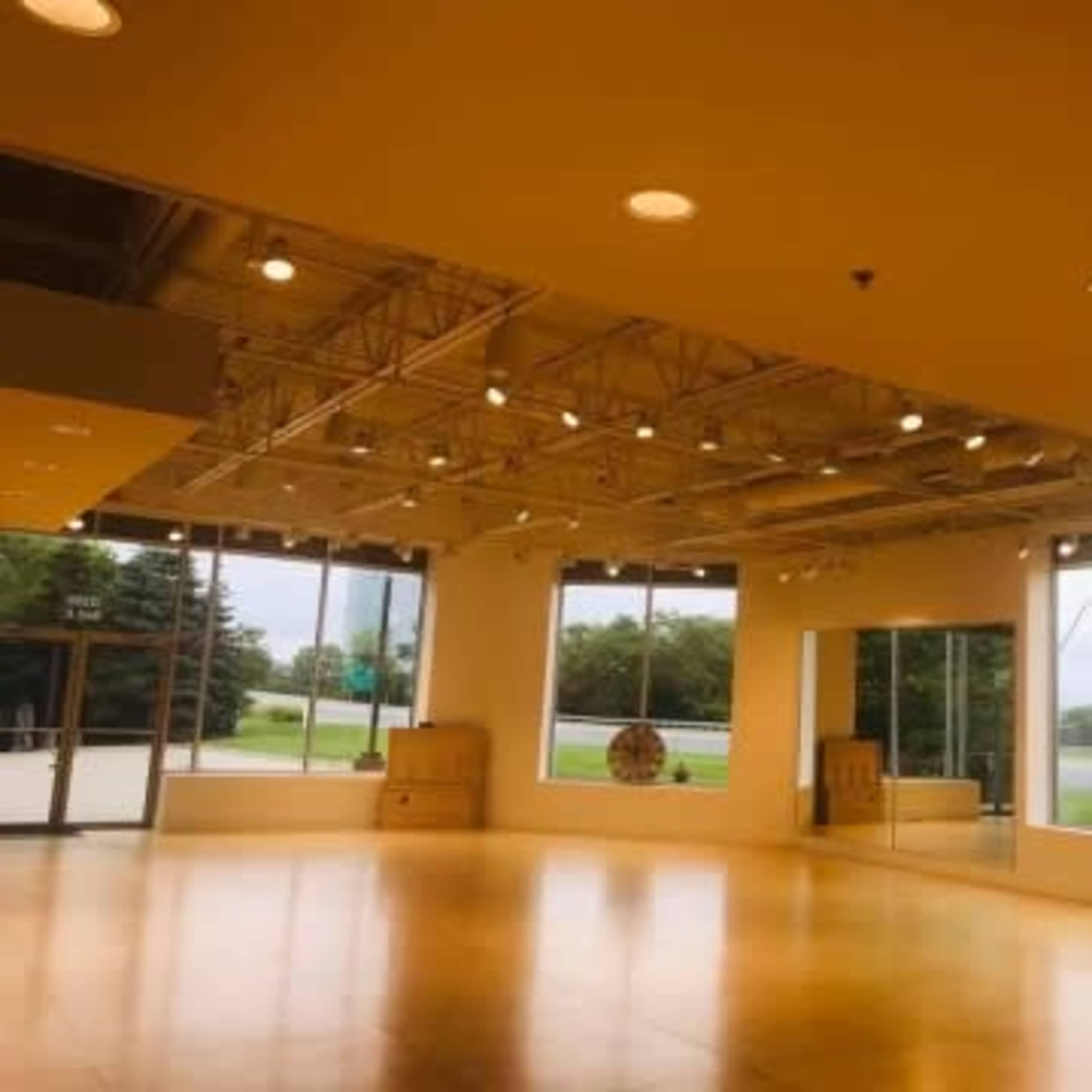 A spacious, brightly lit studio with large windows and a polished wooden floor.