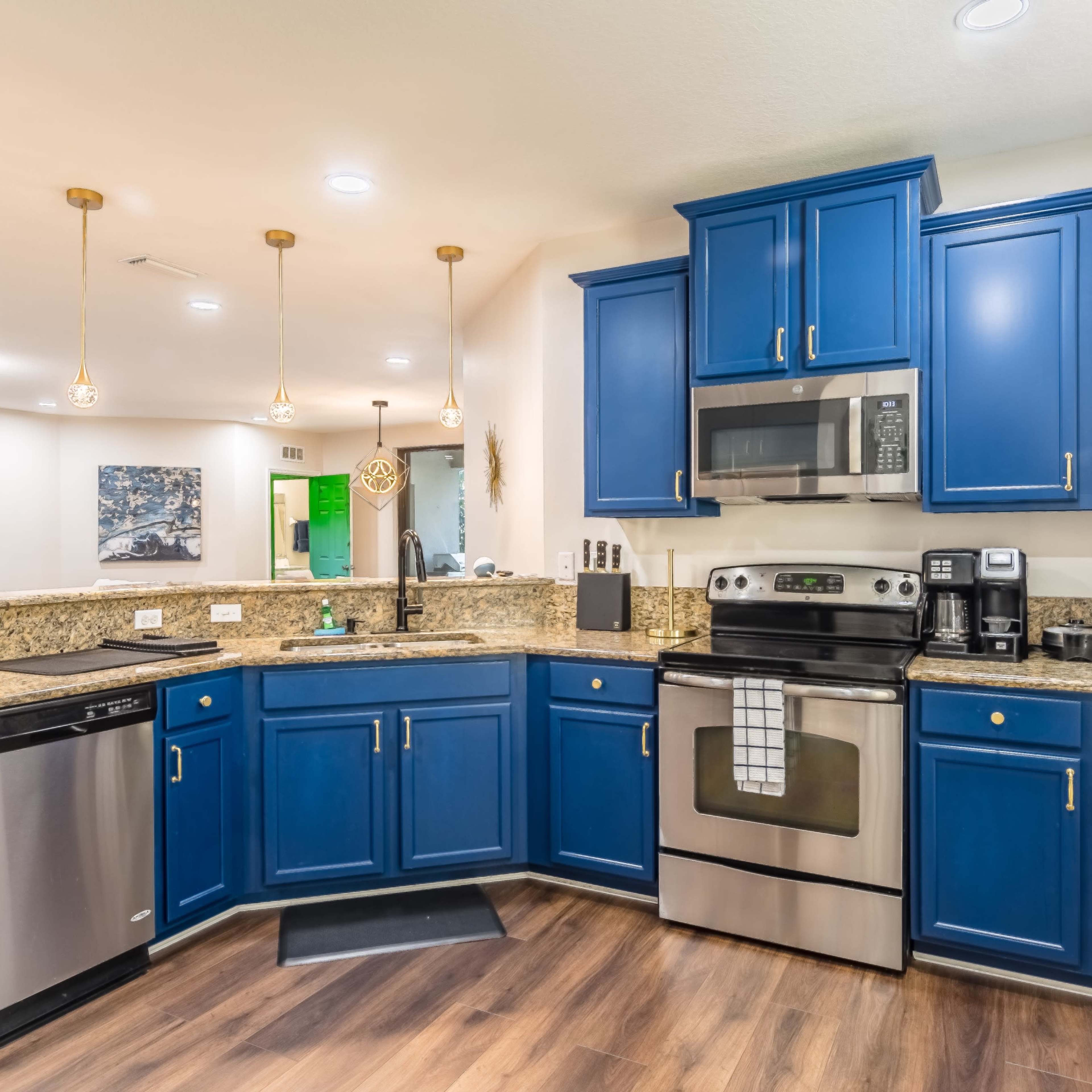 A modern kitchen featuring blue cabinets, granite countertops, stainless steel appliances, and pendant lighting.
