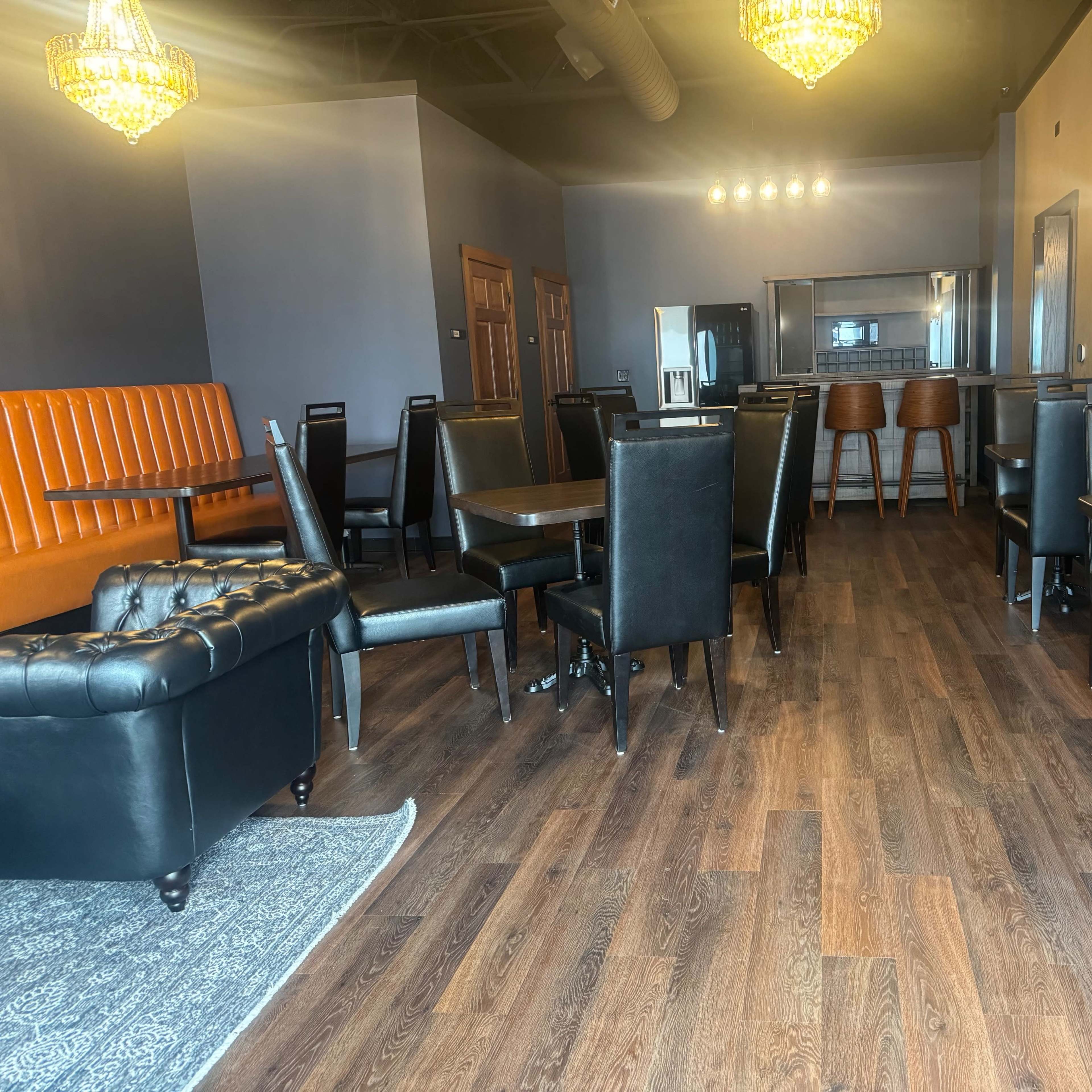 A modern restaurant interior with wooden floors, black seating, and a row of chandeliers overhead.
