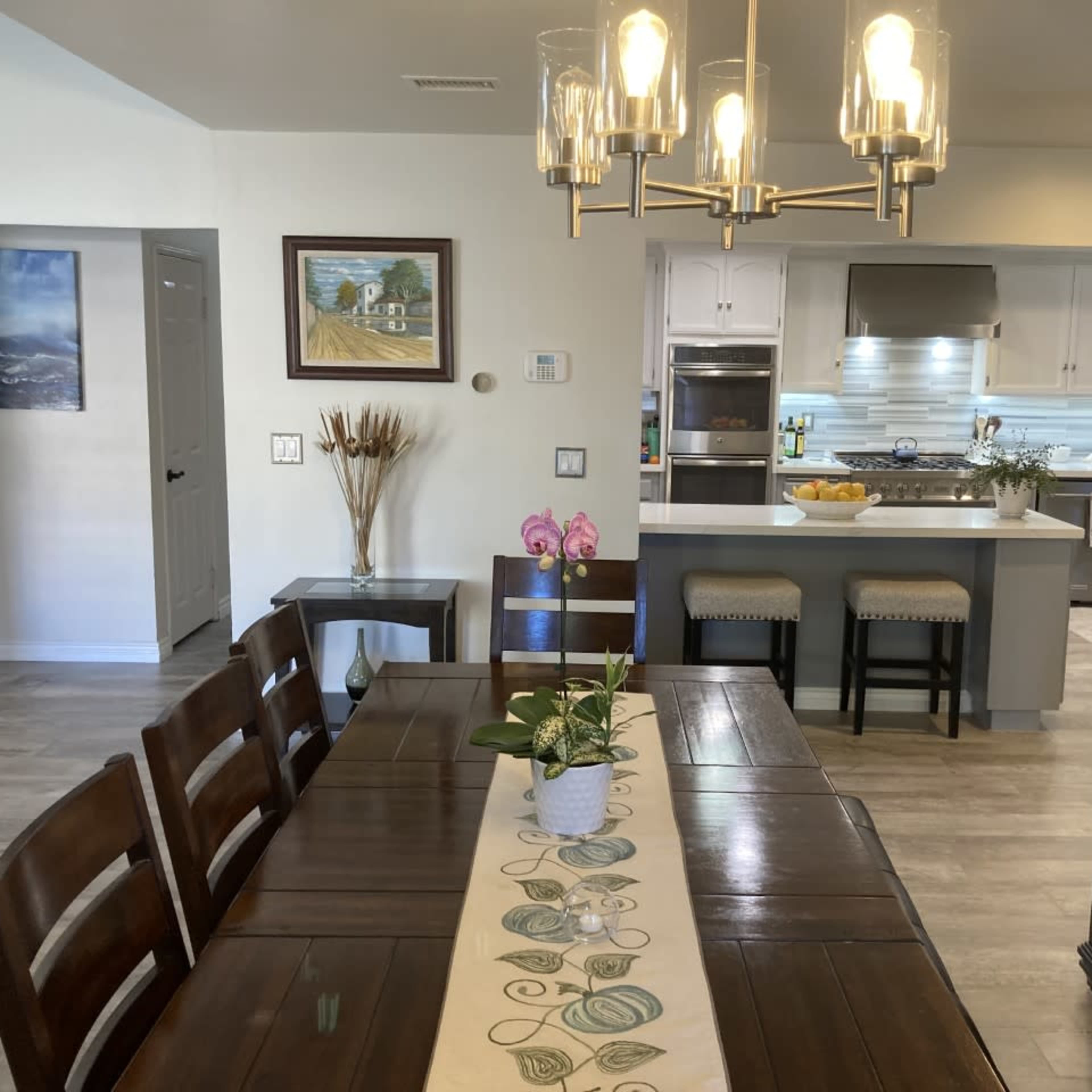 A dining area with a wooden table and chairs is adjacent to a modern kitchen featuring a large island and pendant lighting.