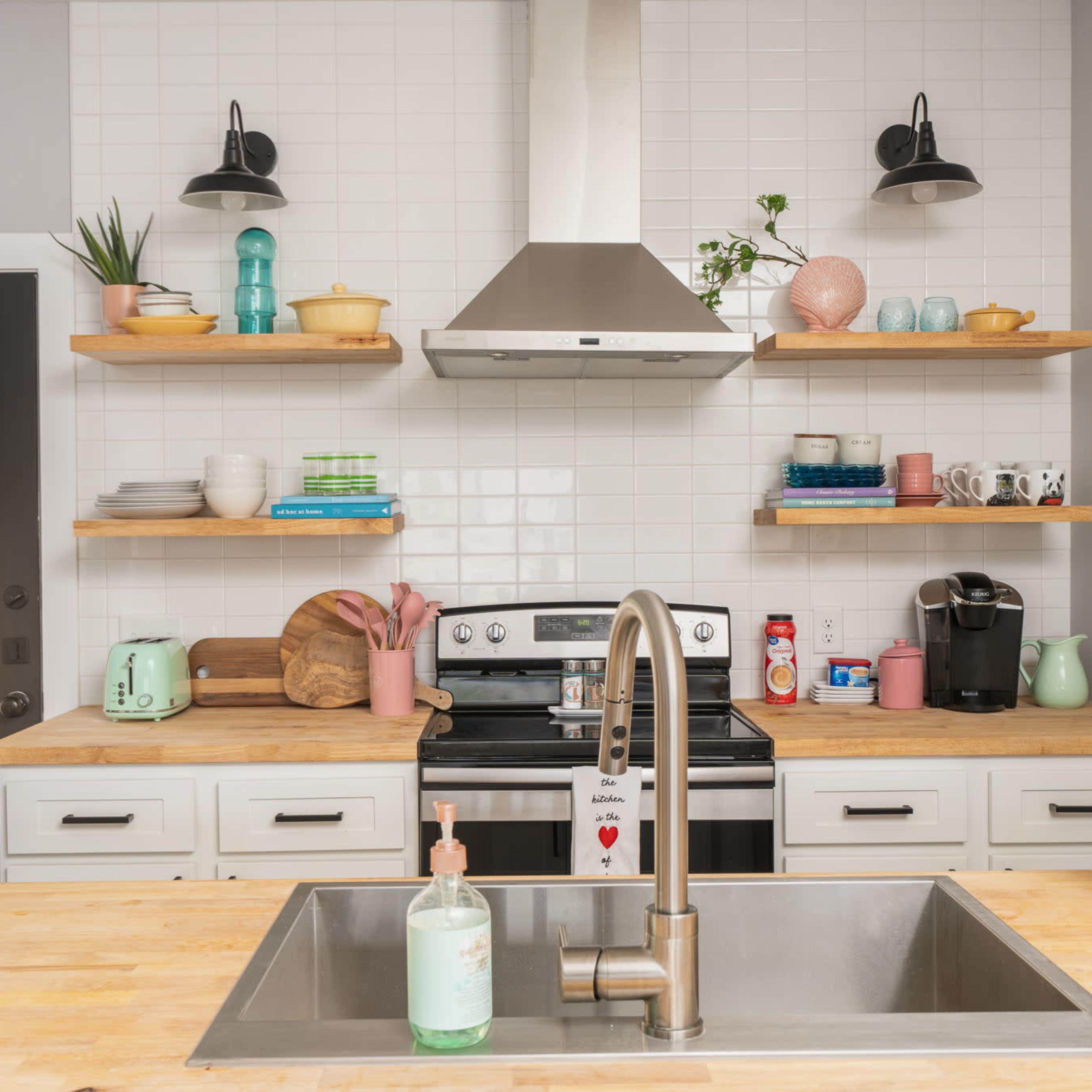 A modern kitchen with a stainless steel stove, open shelving displaying various kitchenware, and a large sink on a wooden countertop.