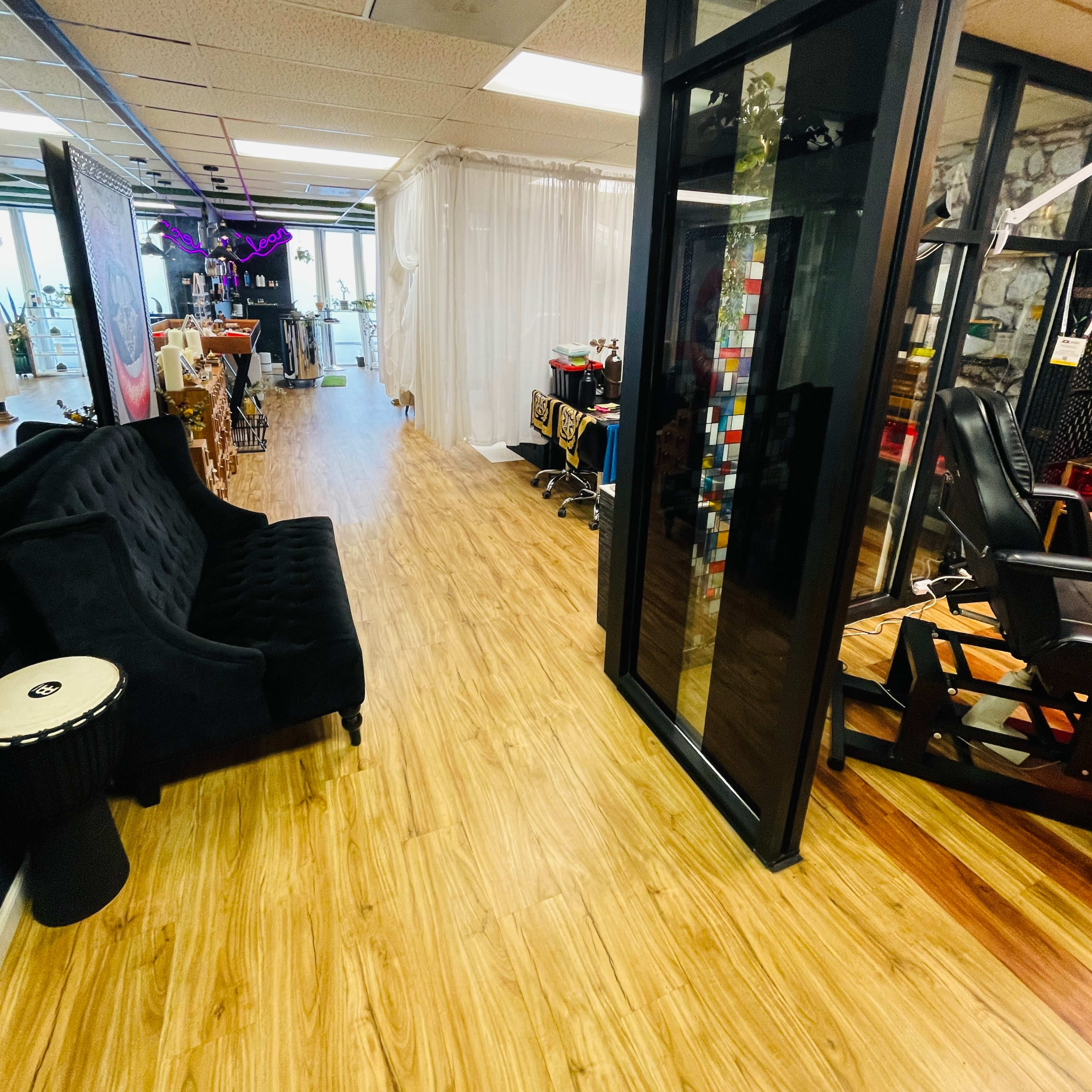 A narrow hallway in a salon with black furniture, wooden flooring, and booths on either side.