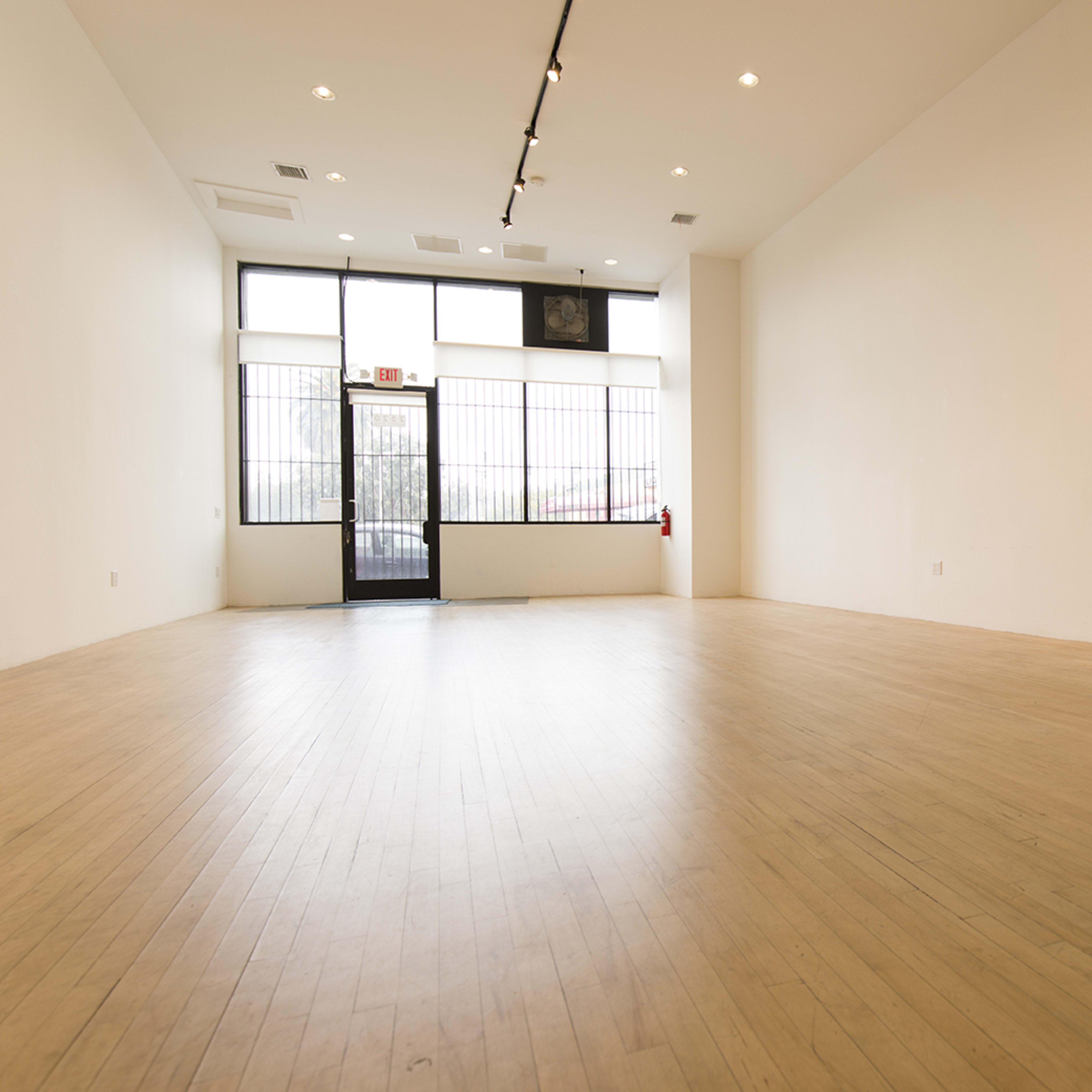 An empty room with wooden flooring and a large window at the entrance.