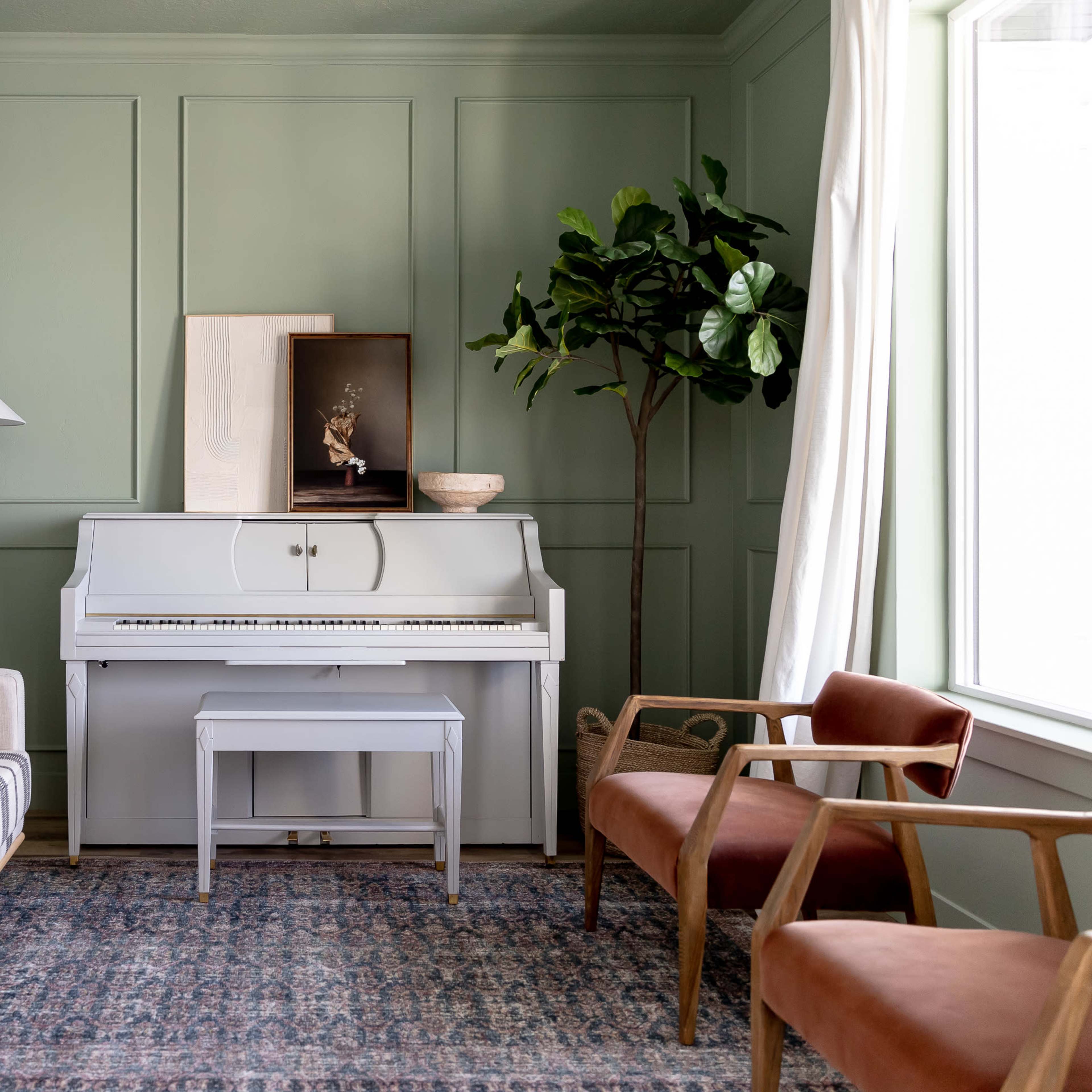 The room features a white piano between two armchairs and a striped sofa, with green walls and a large window letting in natural light.